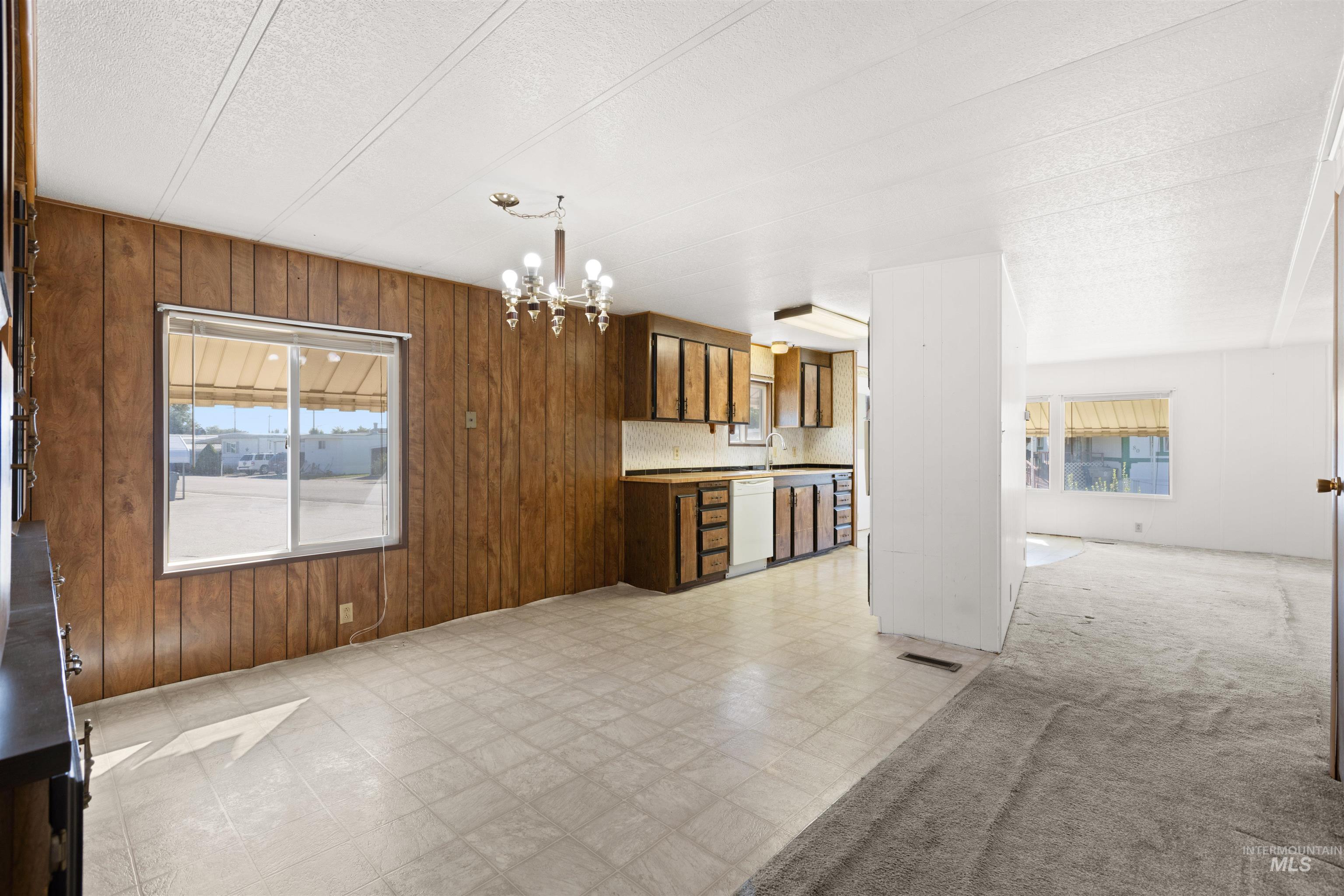 Kitchen with light flooring, wood walls, a chandelier, white dishwasher, and light countertops
