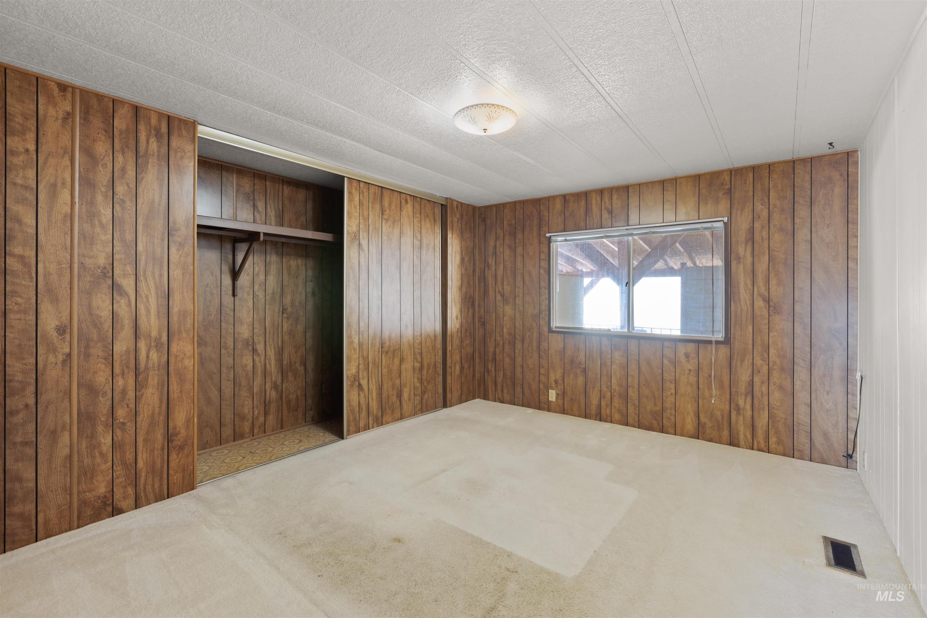 Unfurnished bedroom featuring carpet flooring, a closet, wood walls, and a textured ceiling