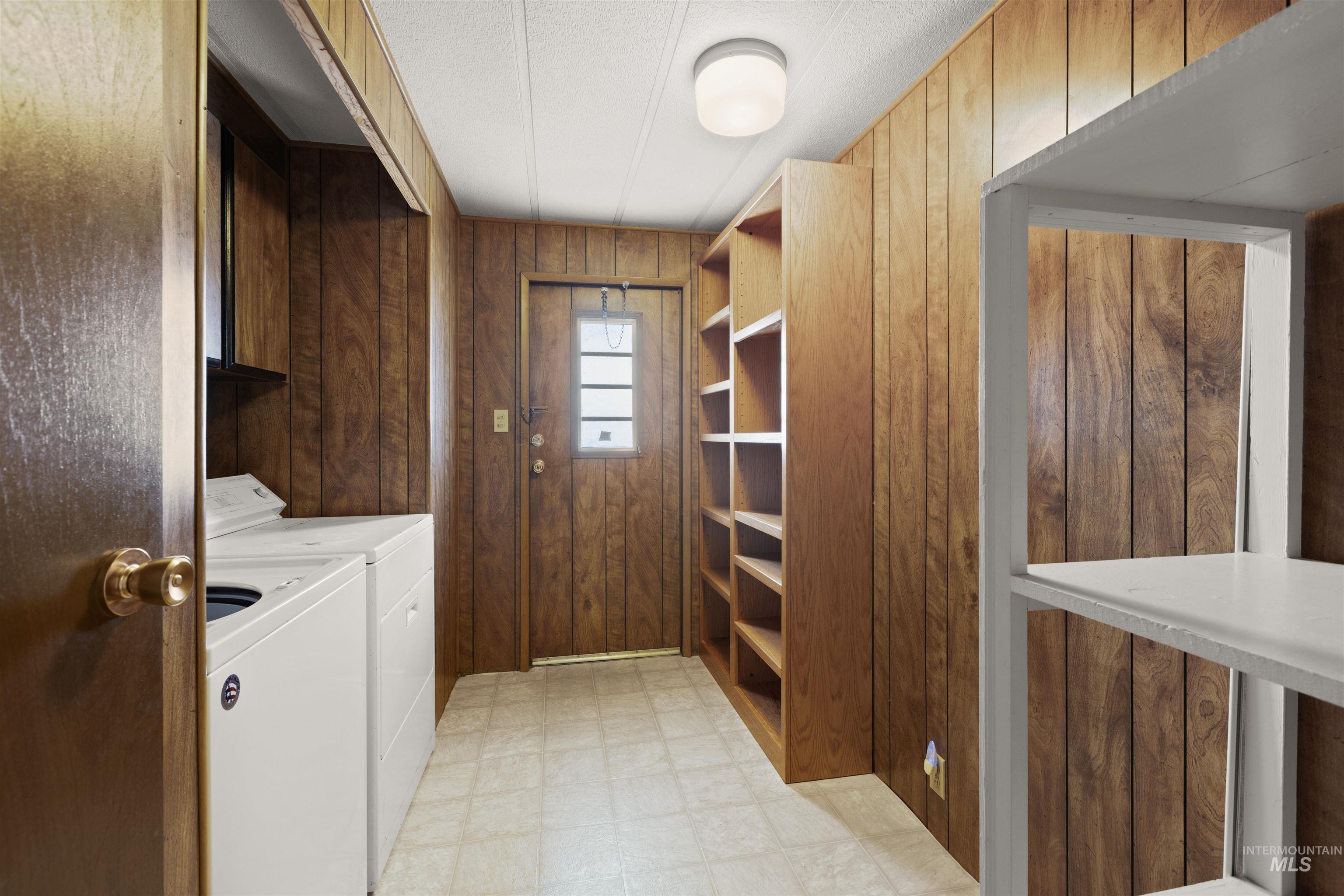Laundry room with wood walls, light floors, and washing machine and clothes dryer