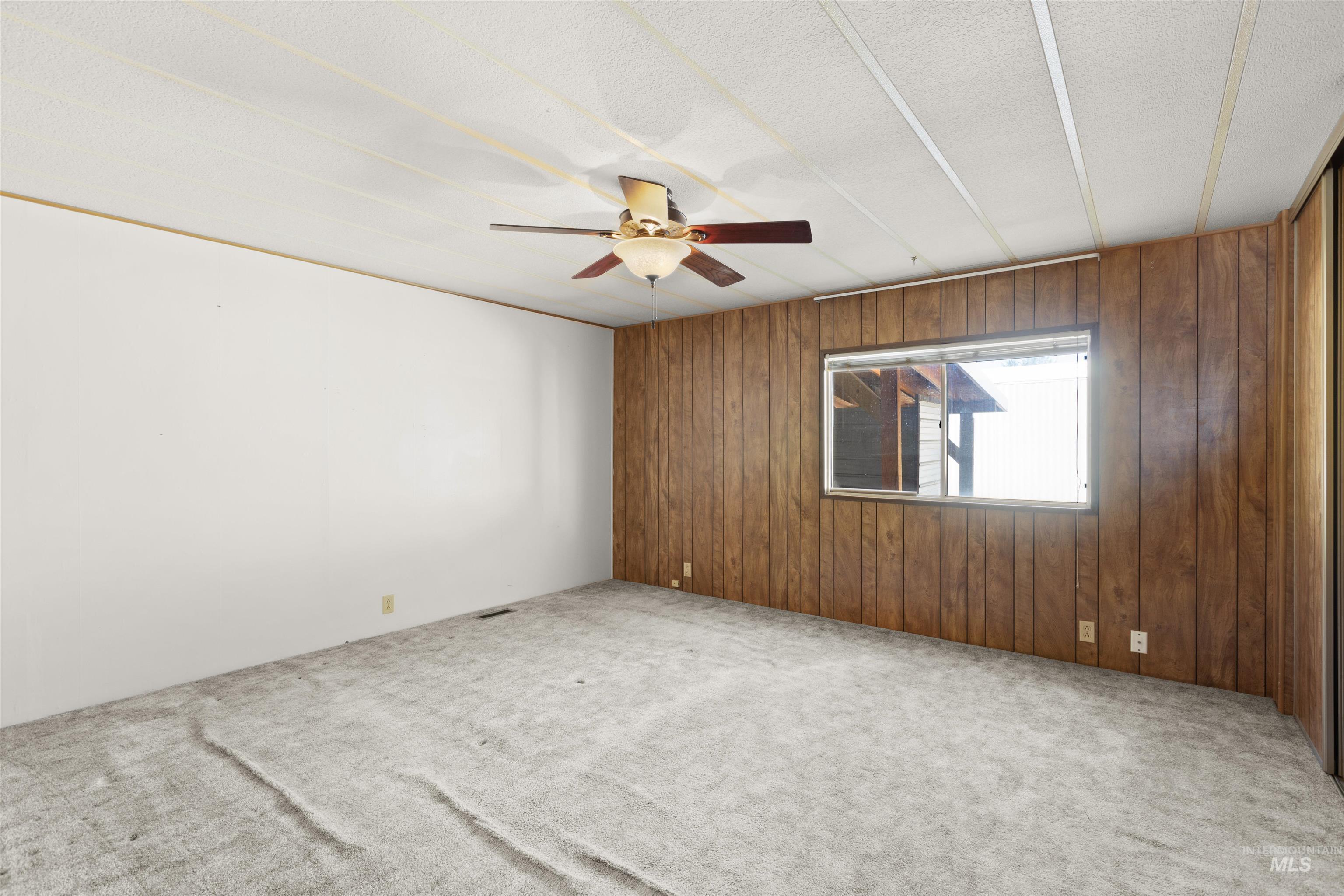 Spare room featuring wood walls, carpet flooring, and a ceiling fan