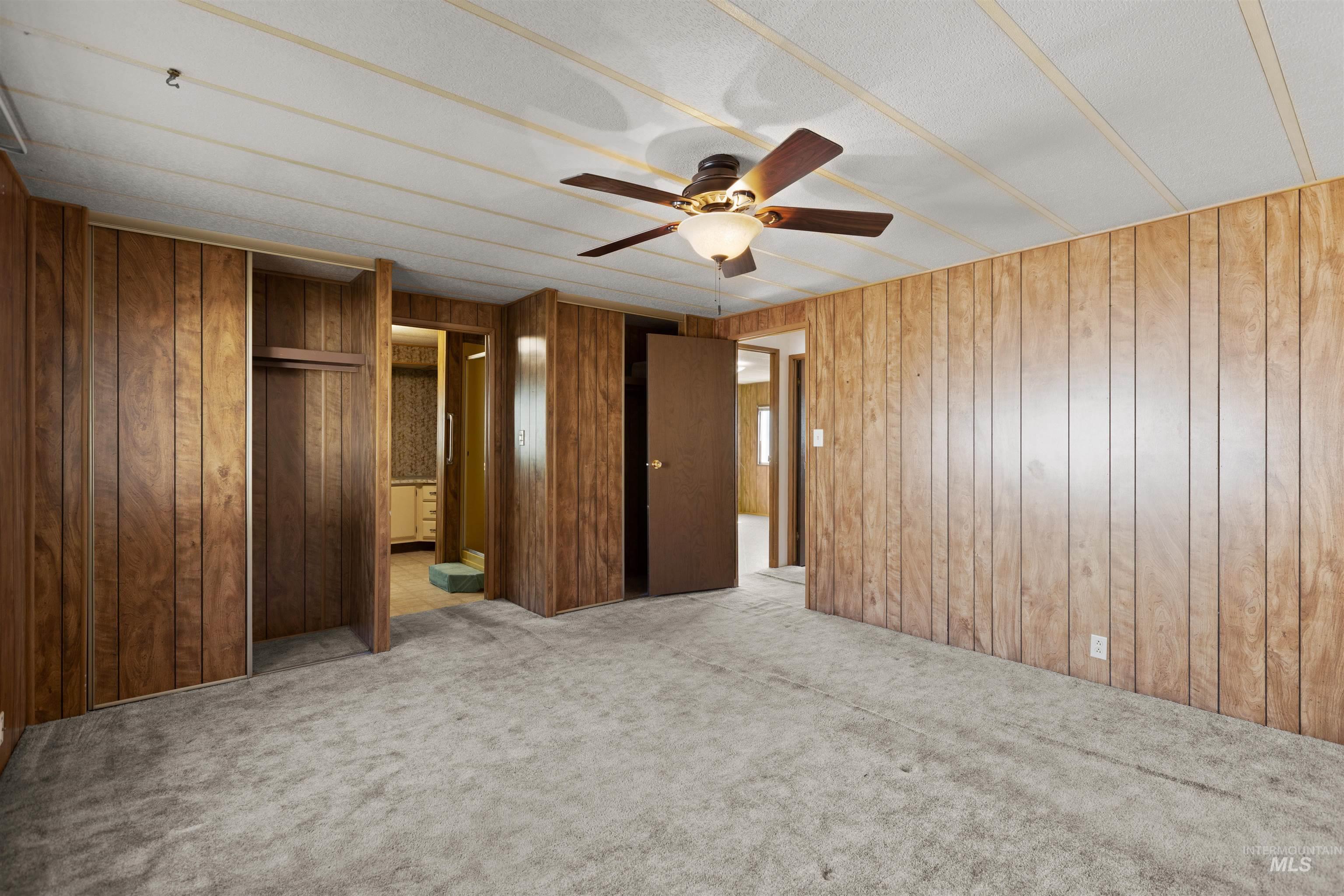 Unfurnished bedroom with light colored carpet, ceiling fan, ensuite bathroom, wood walls, and a closet