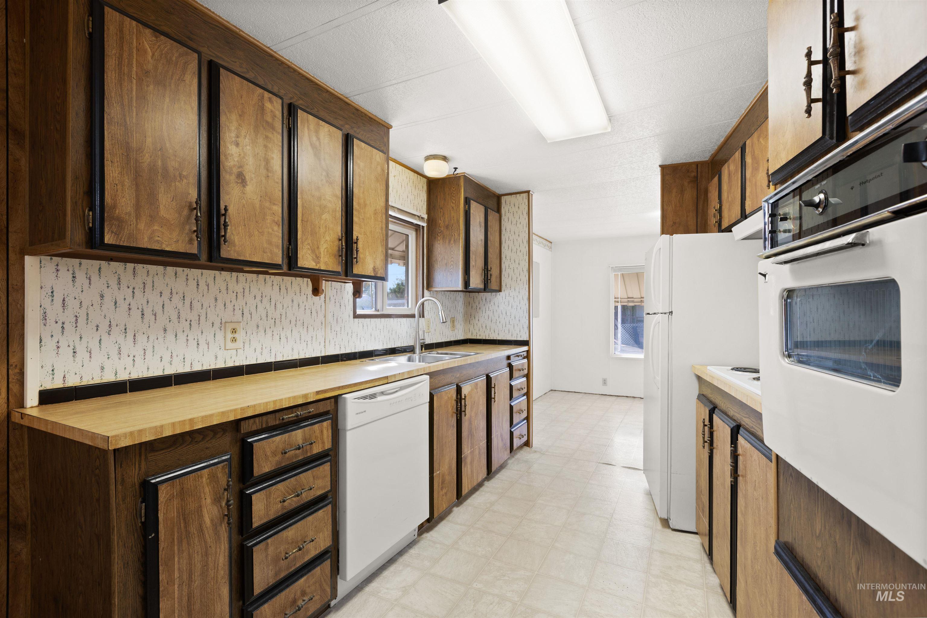 Kitchen featuring light flooring, white appliances, dark brown cabinetry, and under cabinet range hood