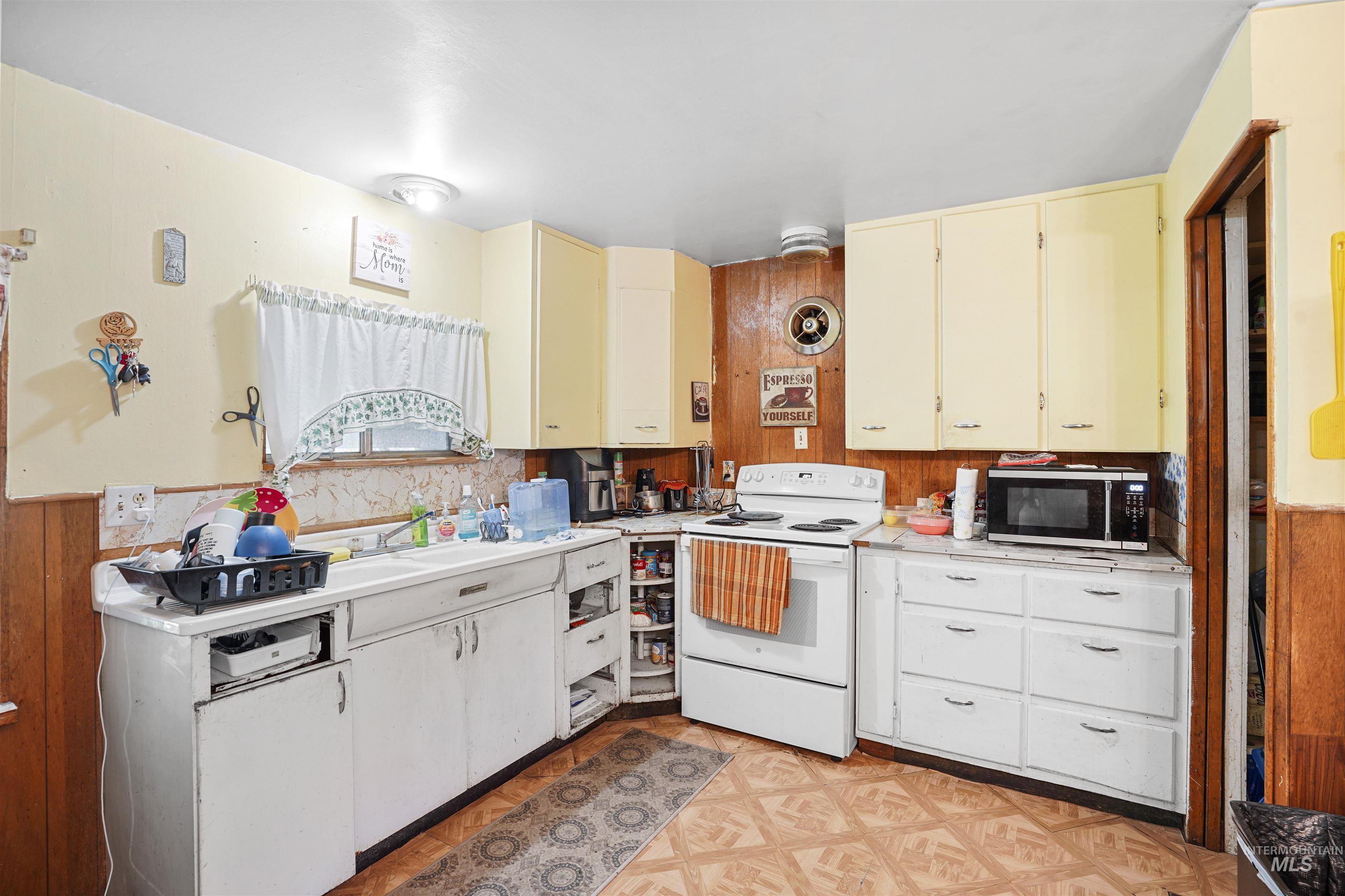 Kitchen featuring light countertops, white electric stove, cream cabinets, stainless steel microwave, and wood walls