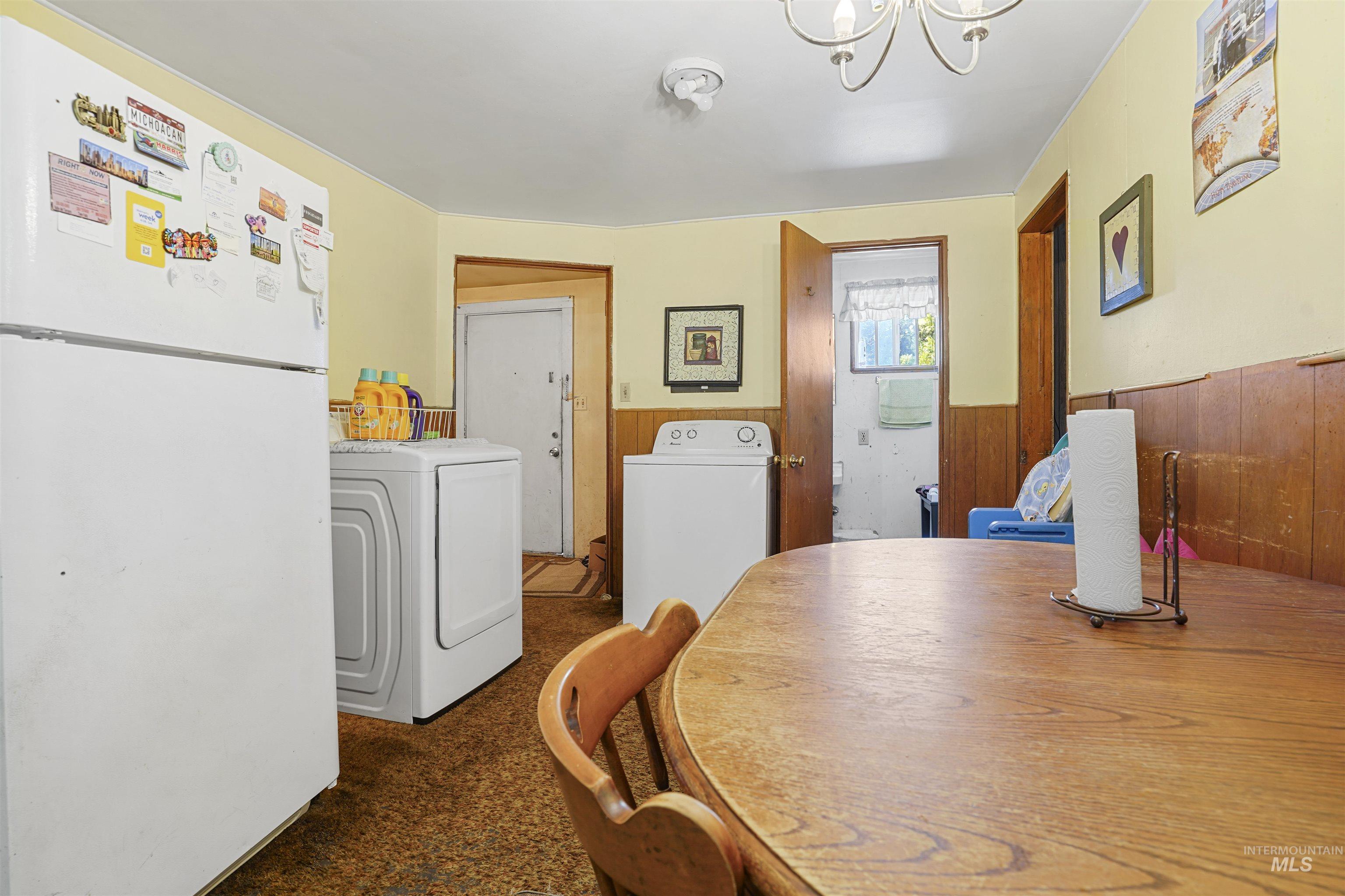 Dining space featuring dark colored carpet, wood walls, washing machine and clothes dryer, a chandelier, and a wainscoted wall