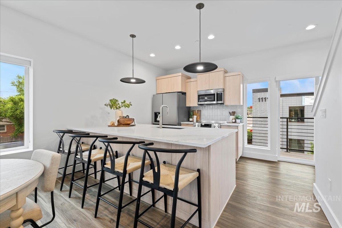 Kitchen featuring light brown cabinetry, wood finished floors, a kitchen breakfast bar, appliances with stainless steel finishes, and decorative backsplash