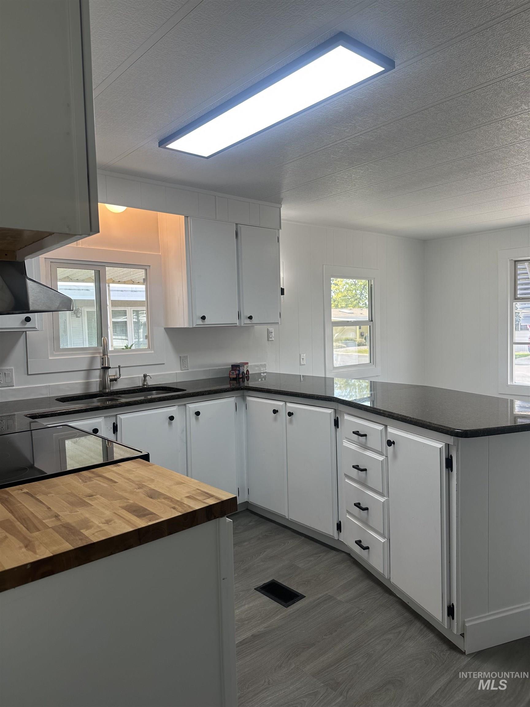 Kitchen featuring a peninsula, white cabinets, dark wood-style floors, black range with electric stovetop, and a textured ceiling