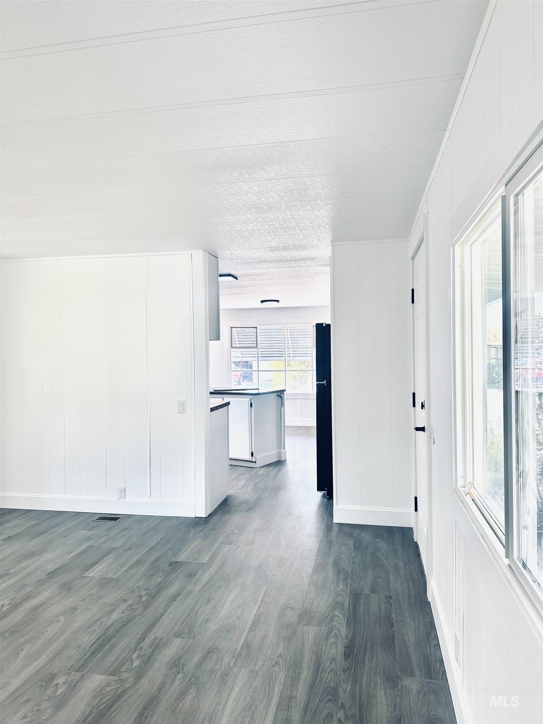Unfurnished living room featuring dark wood-type flooring and a decorative wall