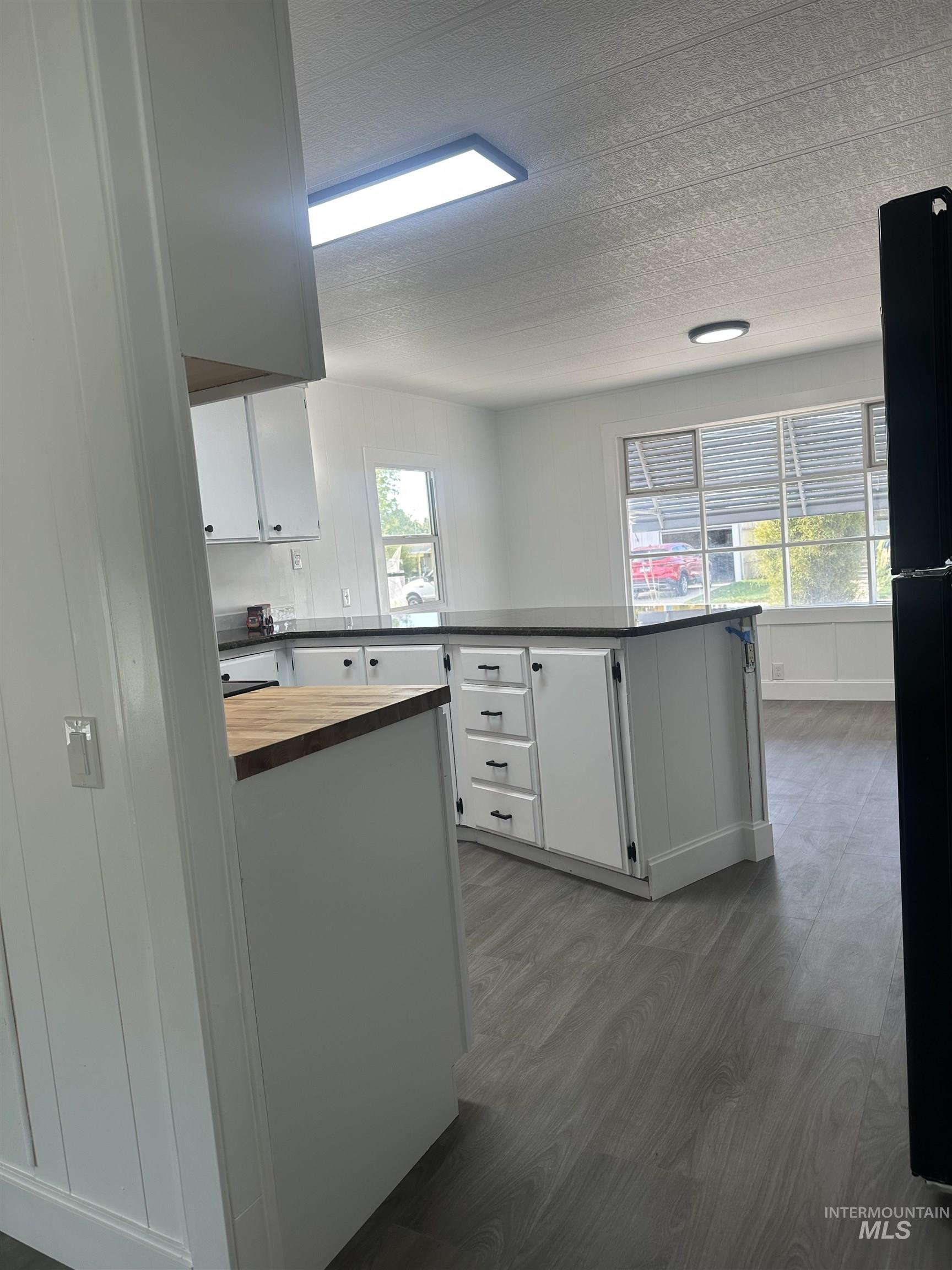 Kitchen featuring dark wood-style floors, a peninsula, wood counters, white cabinets, and a textured ceiling
