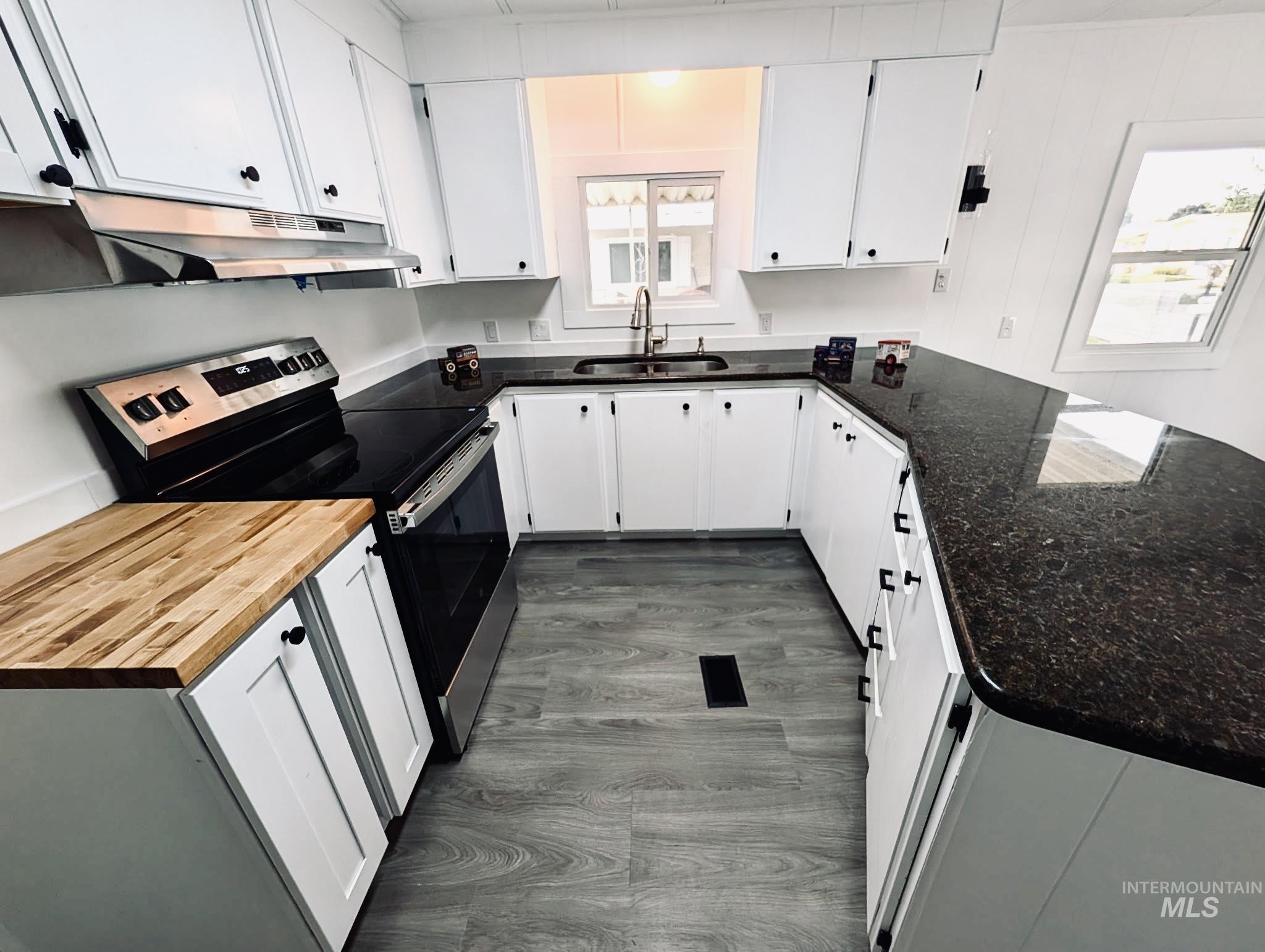 Kitchen featuring stainless steel range with electric cooktop, white cabinetry, dark wood finished floors, and a peninsula