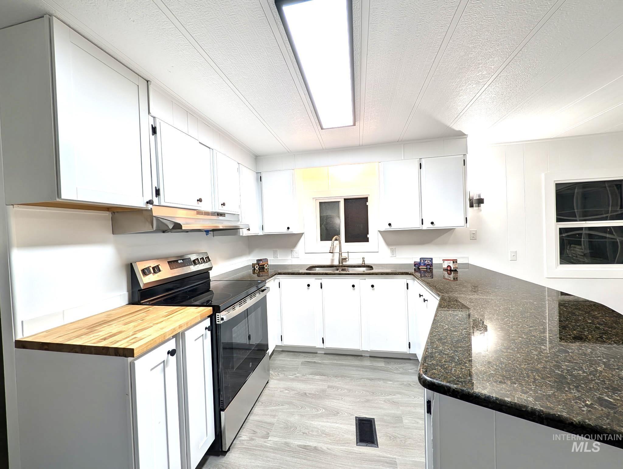 Kitchen with electric stove, a textured ceiling, white cabinets, light wood-style flooring, and under cabinet range hood