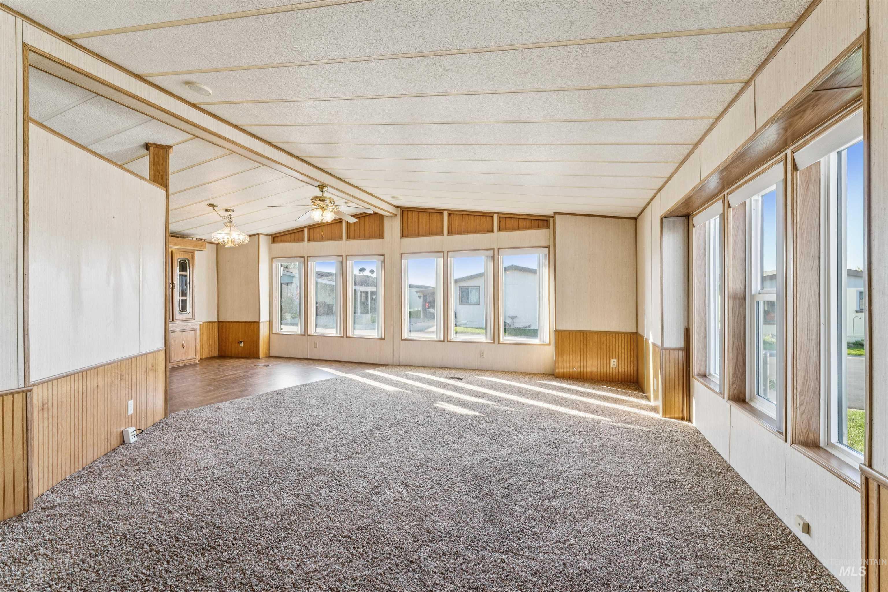 Carpeted spare room featuring wood walls, a wainscoted wall, and a ceiling fan