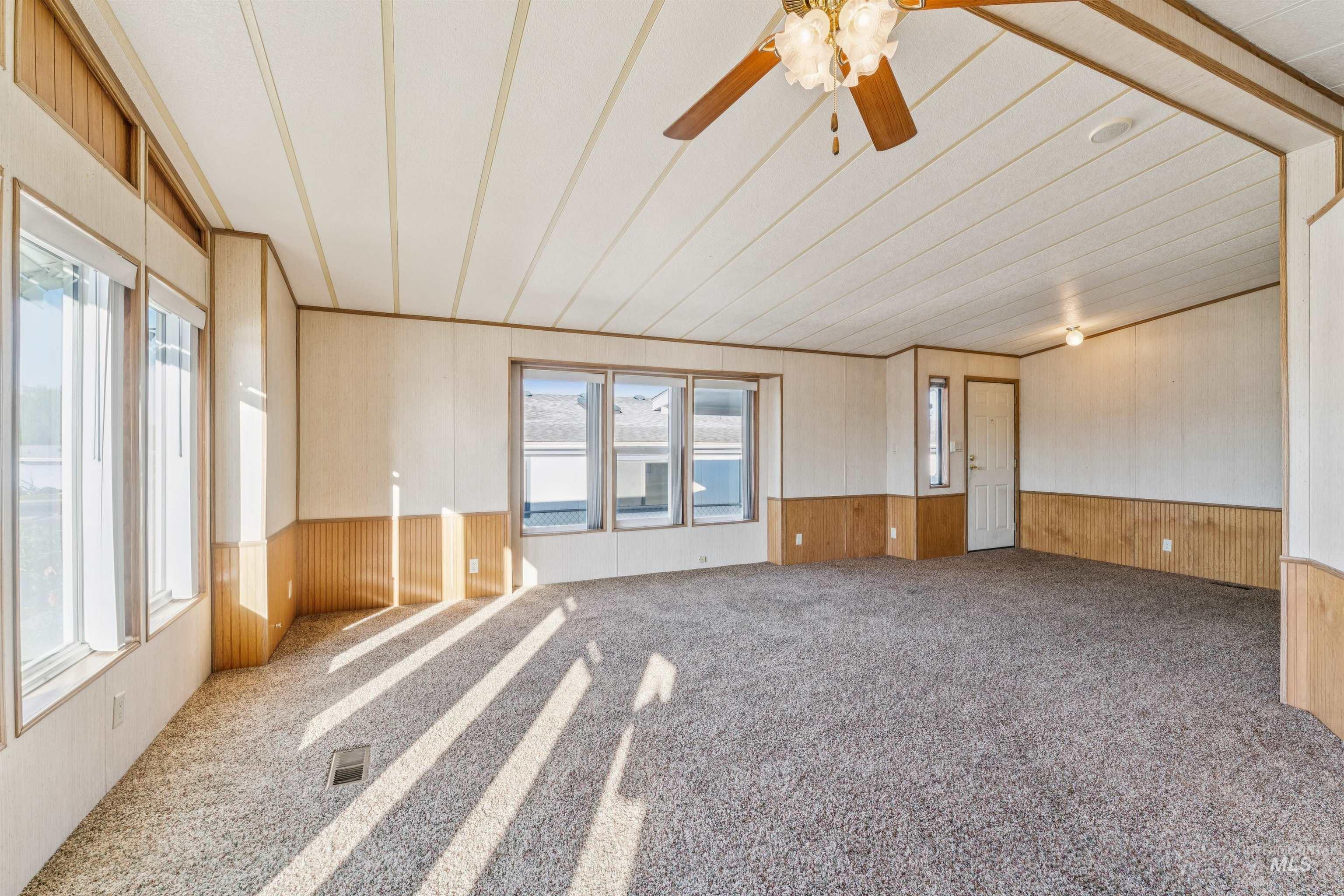 Carpeted spare room featuring wood walls, a wainscoted wall, and ceiling fan