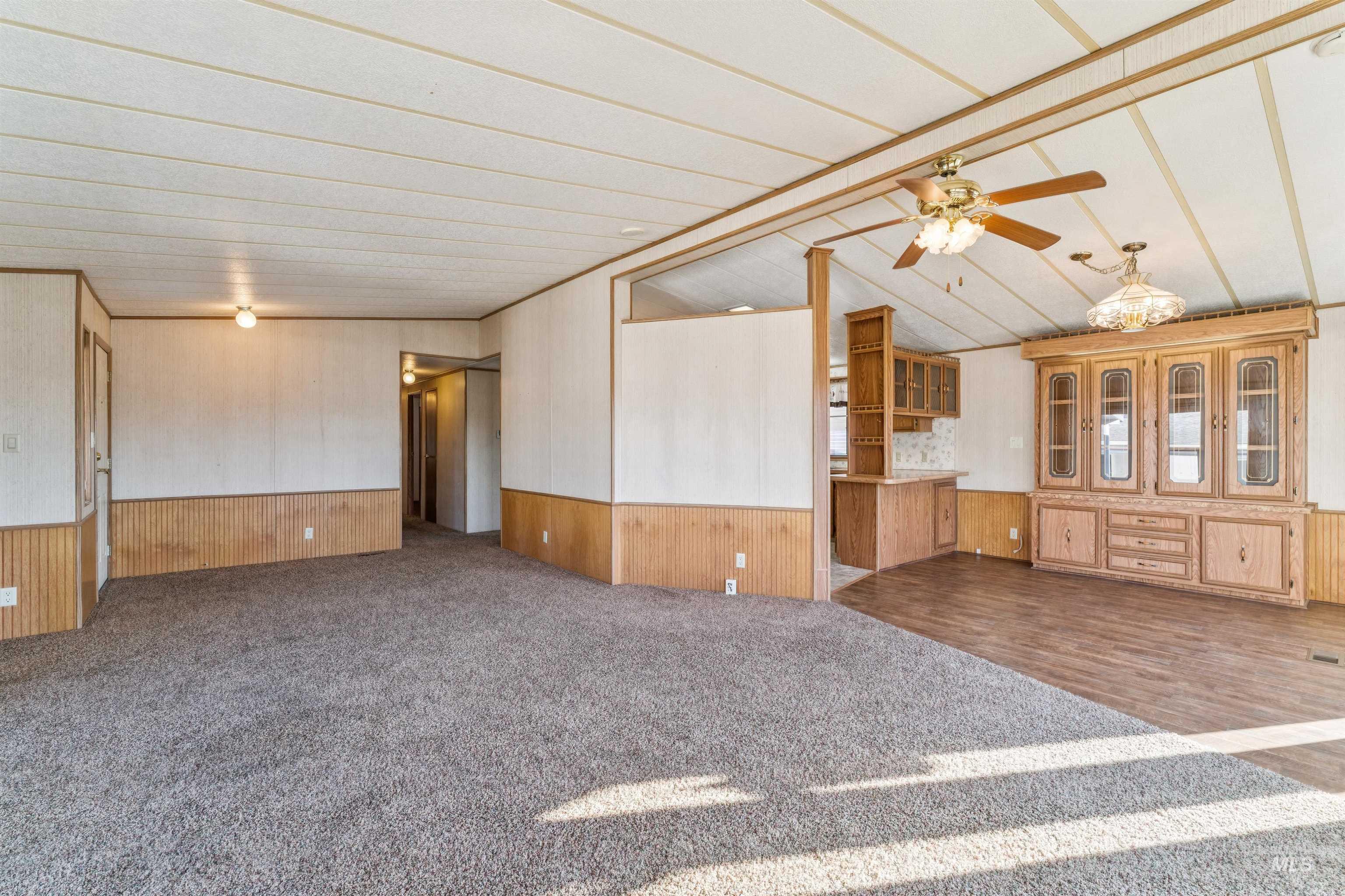 Unfurnished living room featuring a wainscoted wall, wood walls, ceiling fan, and dark colored carpet