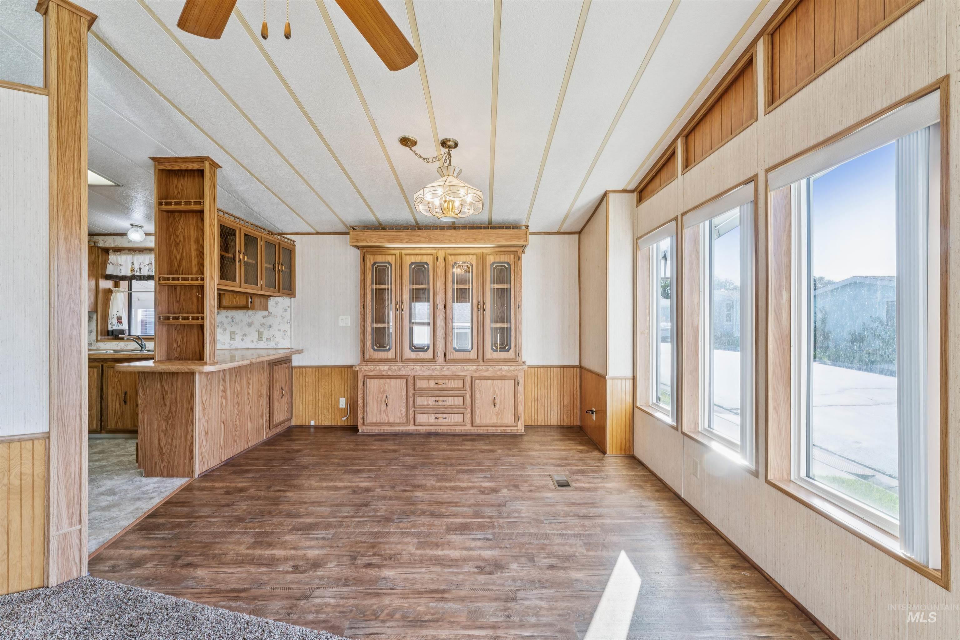 Unfurnished dining area featuring wooden walls, wainscoting, dark wood finished floors, and ceiling fan