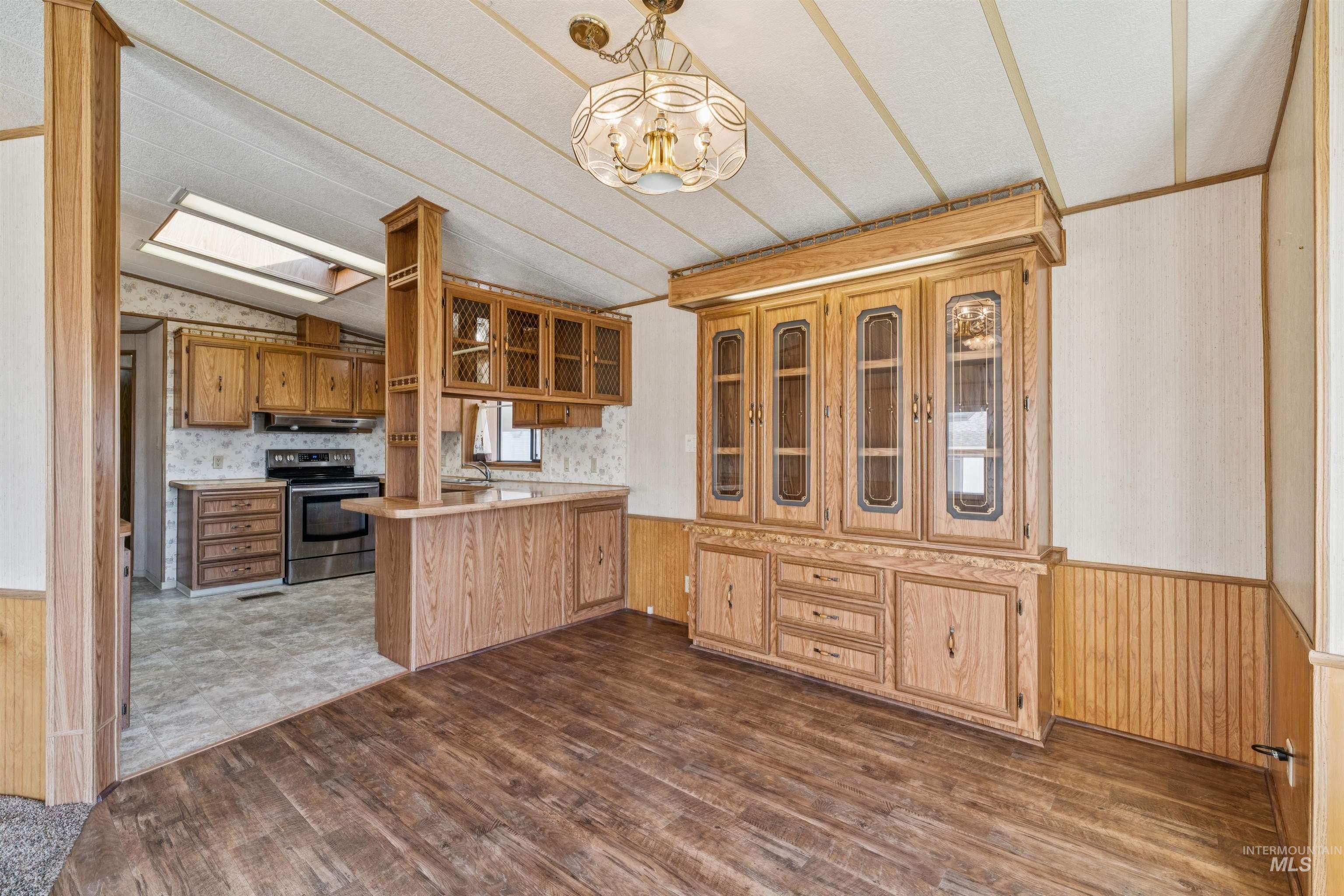 Kitchen featuring wainscoting, wooden walls, wallpapered walls, a peninsula, and decorative light fixtures