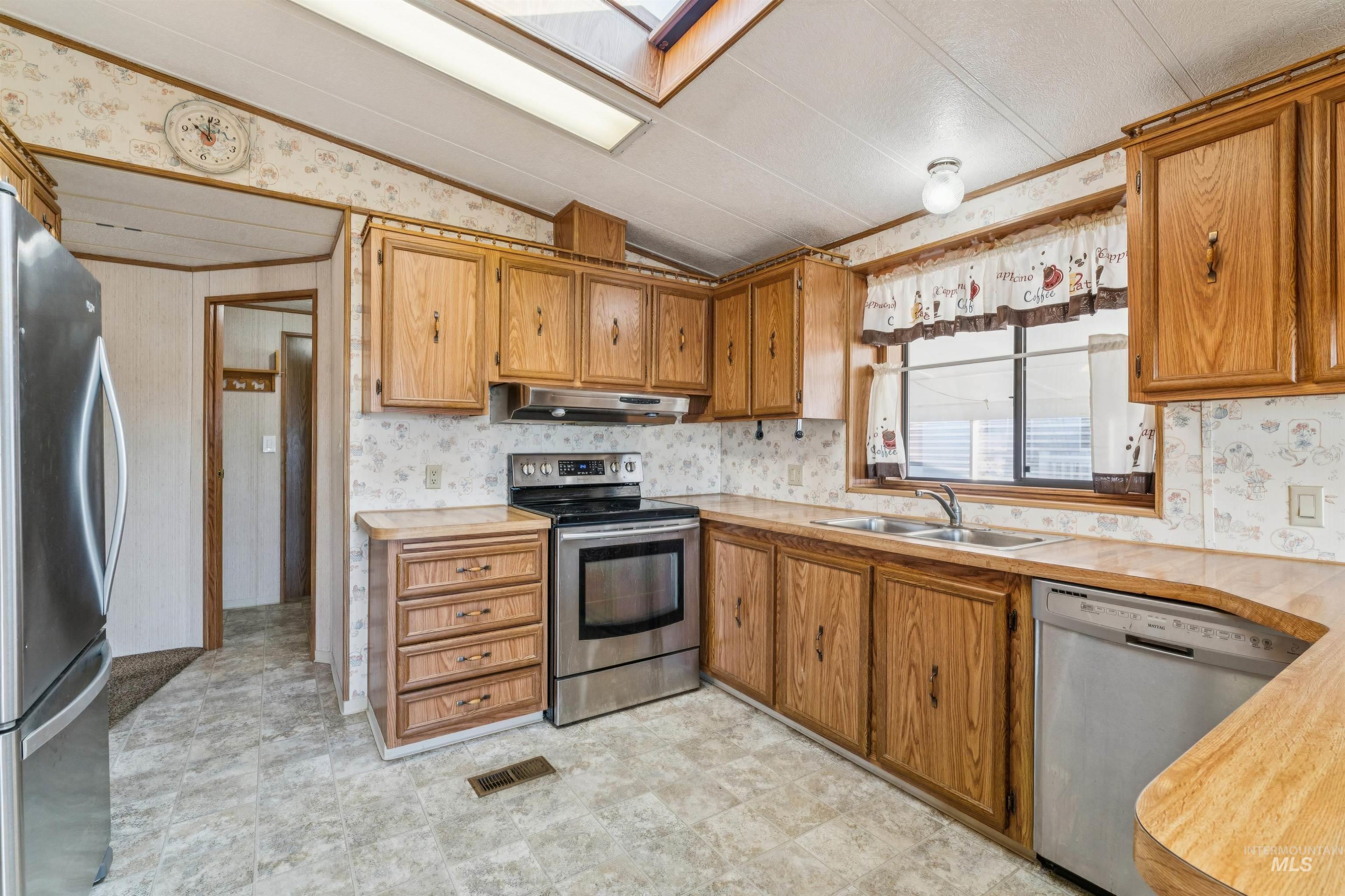 Kitchen featuring wallpapered walls, vaulted ceiling, appliances with stainless steel finishes, light countertops, and a skylight