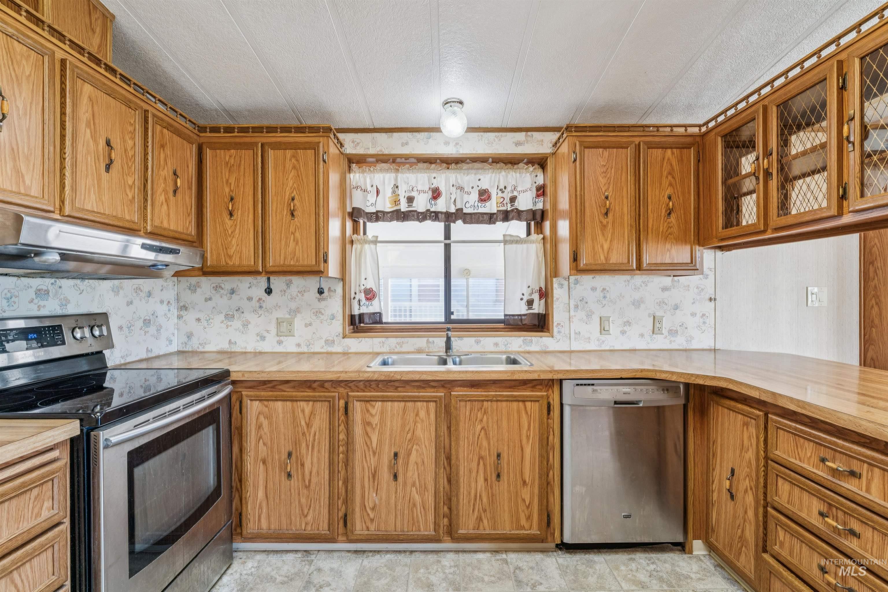 Kitchen featuring stainless steel appliances, light countertops, brown cabinets, under cabinet range hood, and a textured ceiling