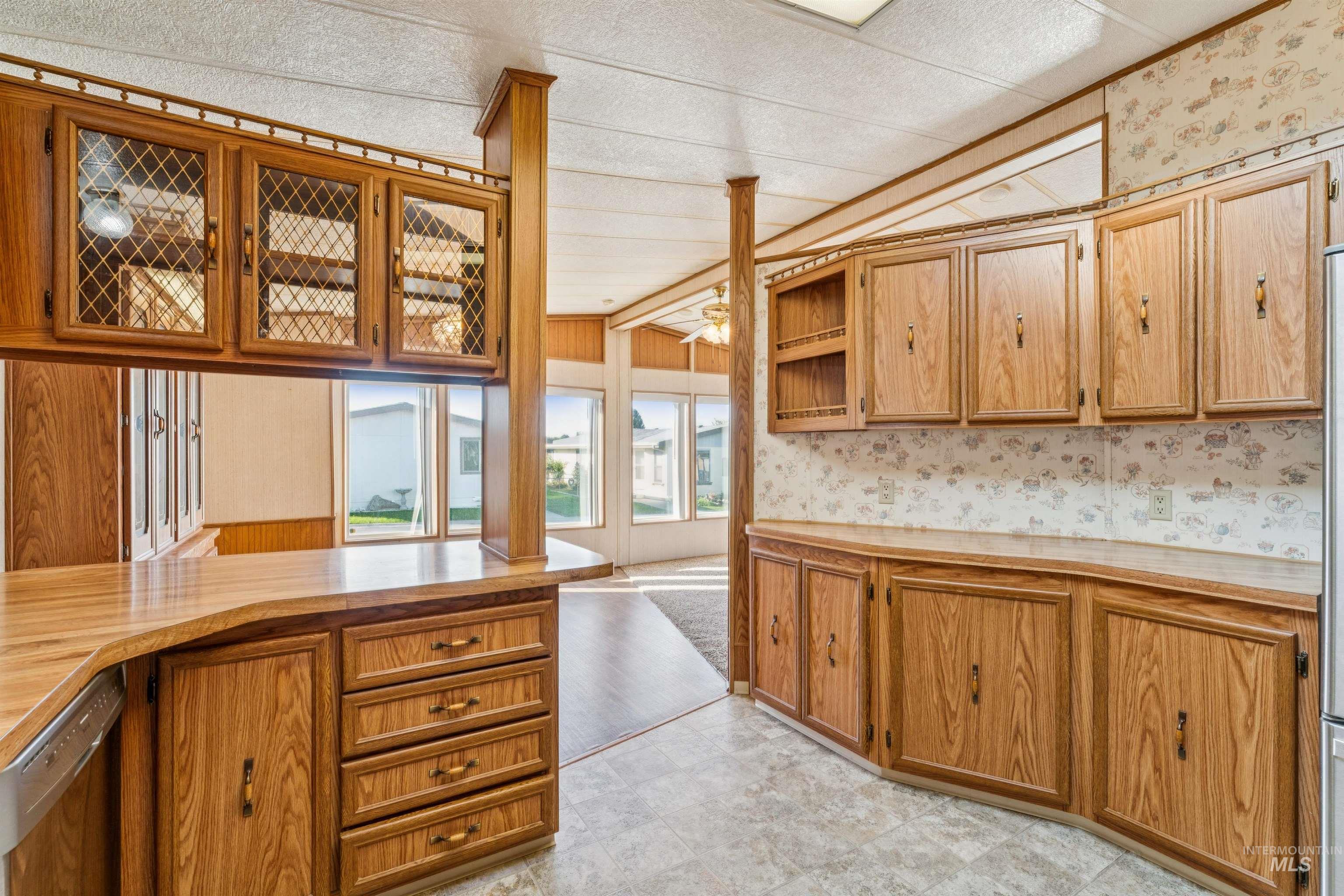 Kitchen with wallpapered walls, light countertops, dishwashing machine, brown cabinetry, and open shelves