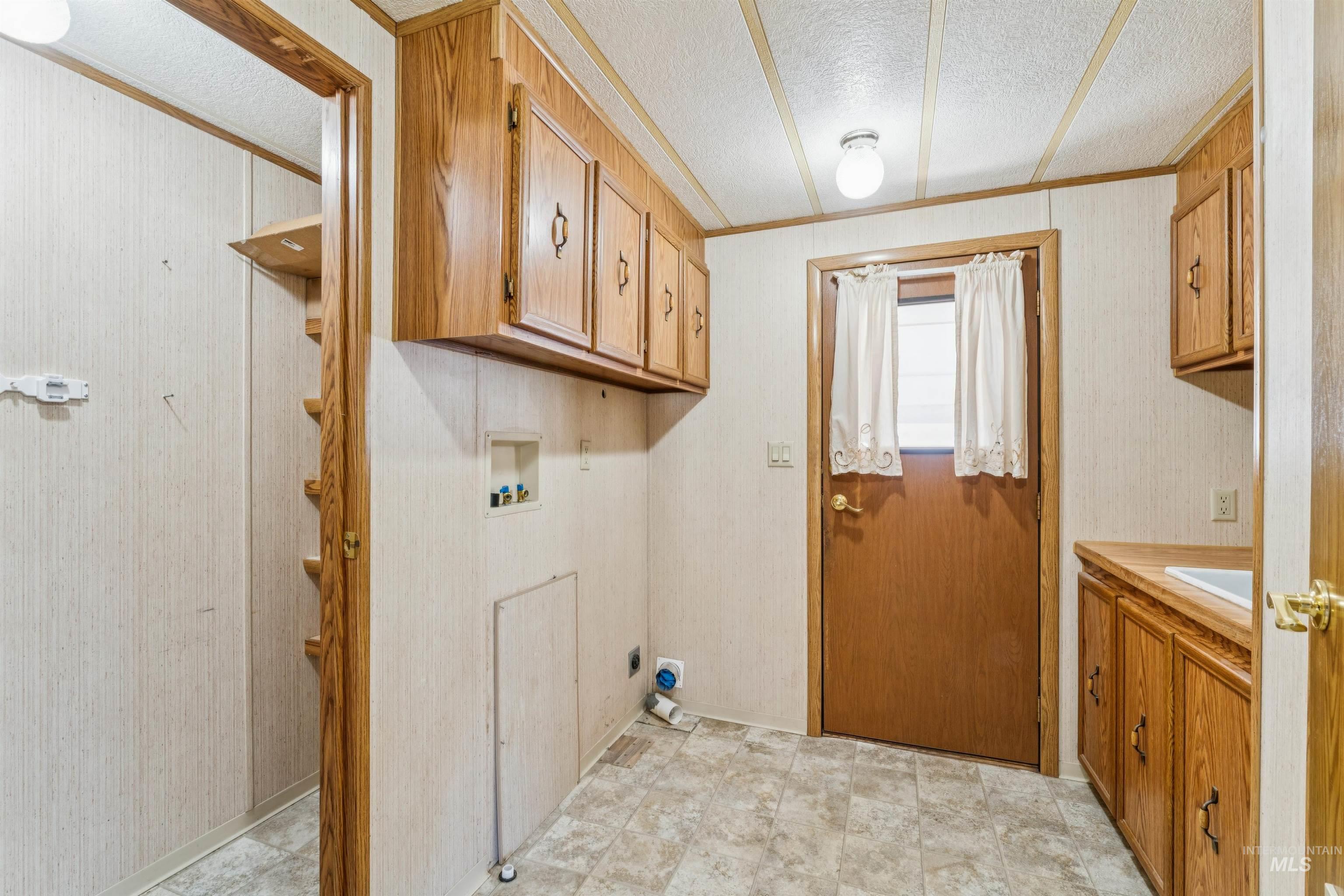 Laundry room featuring wallpapered walls, a textured ceiling, crown molding, washer hookup, and cabinet space