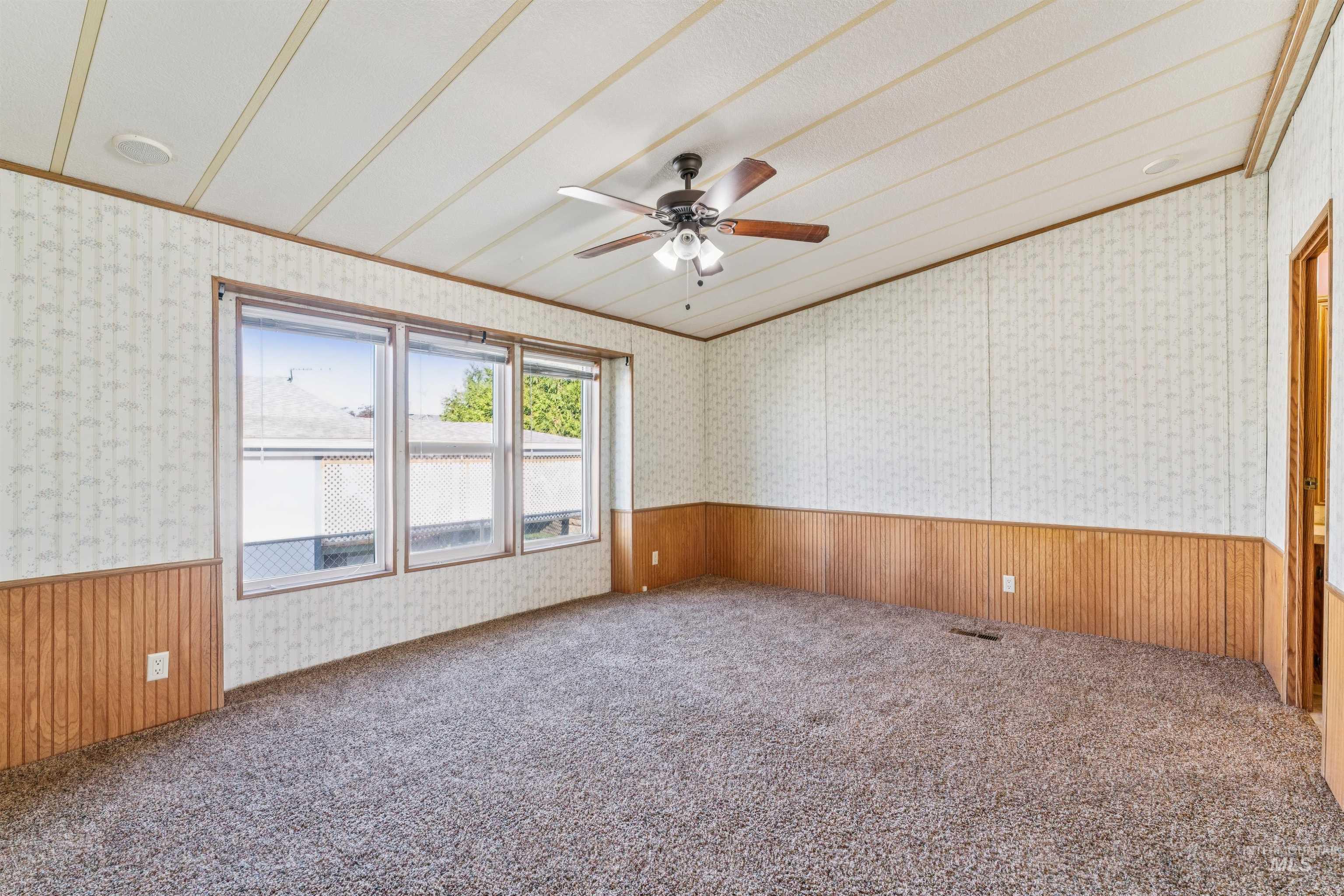 Carpeted spare room with wainscoting, wallpapered walls, crown molding, wood walls, and ceiling fan