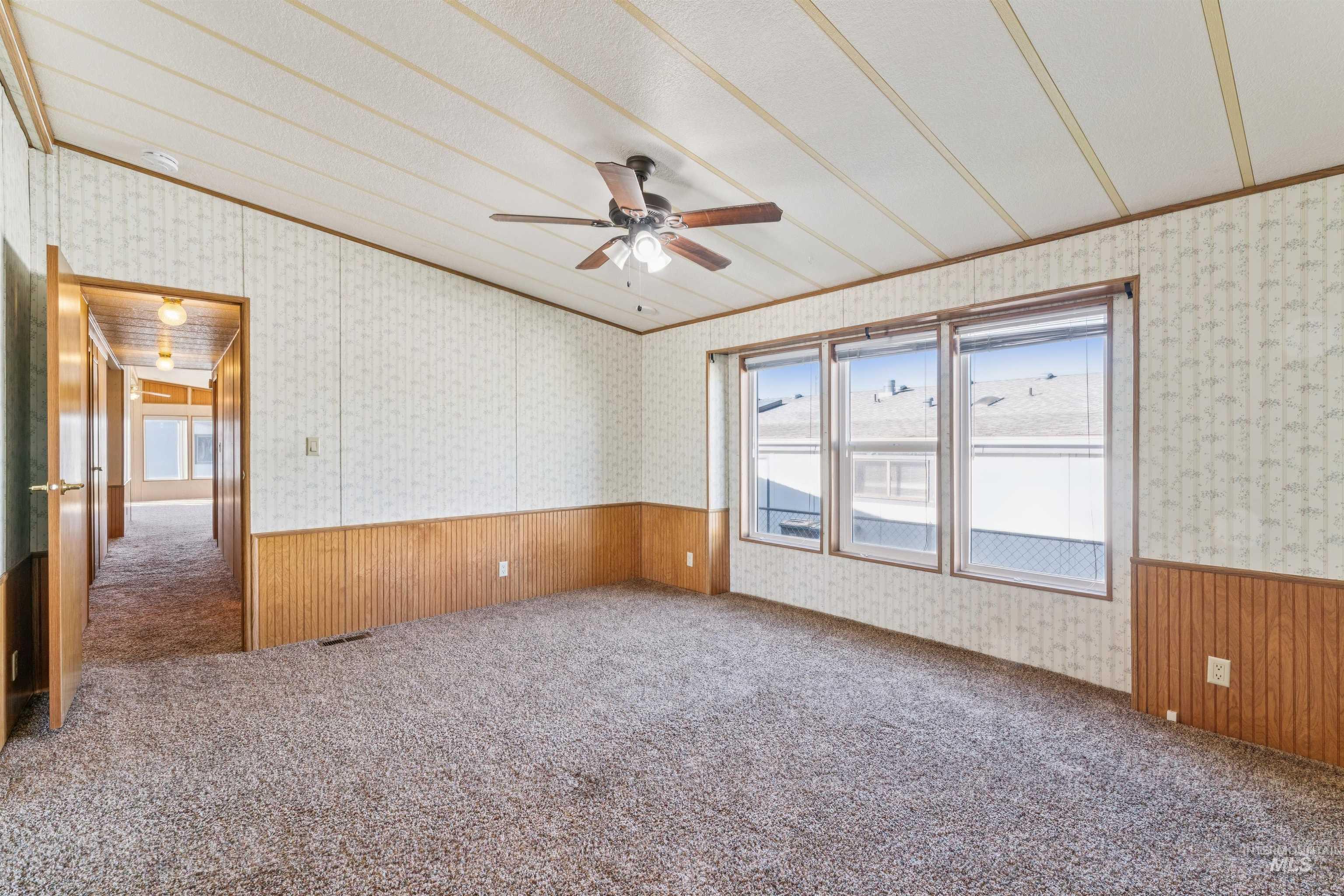 Carpeted empty room with plenty of natural light, wainscoting, wooden walls, wallpapered walls, and a ceiling fan