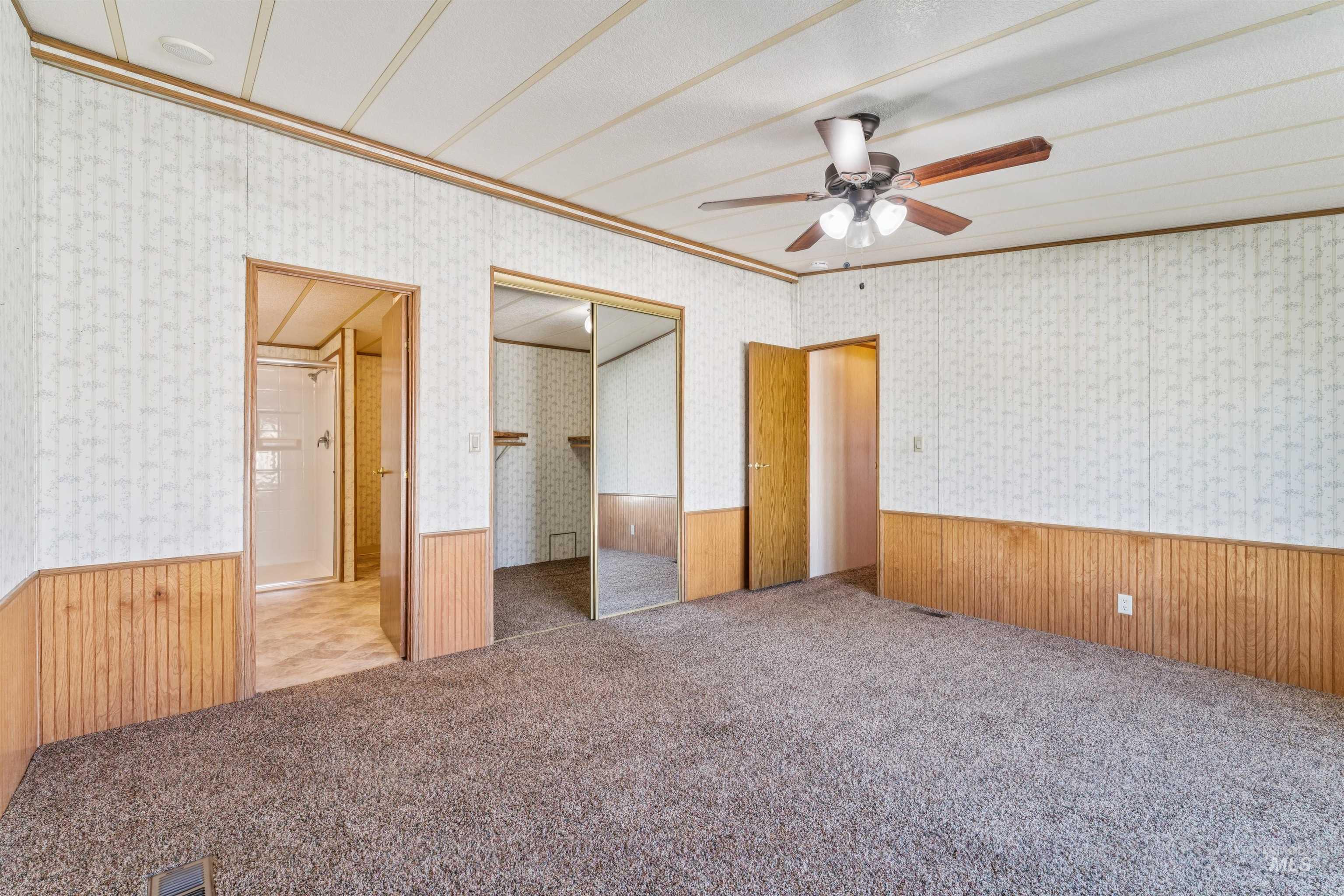 Unfurnished bedroom with wainscoting, wood walls, ornamental molding, carpet, and a ceiling fan