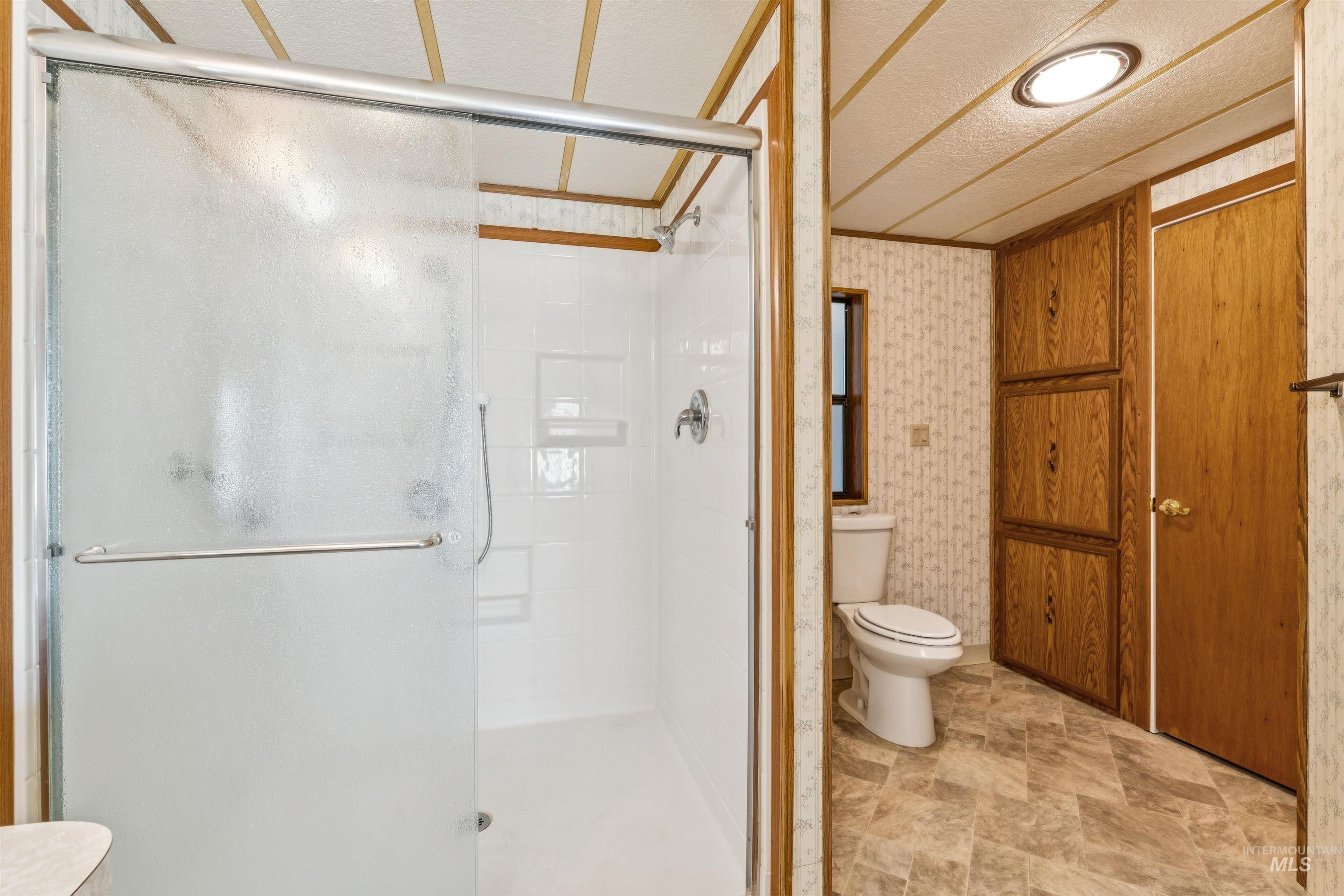 Full bath with a stall shower, stone finish flooring, and wallpapered walls