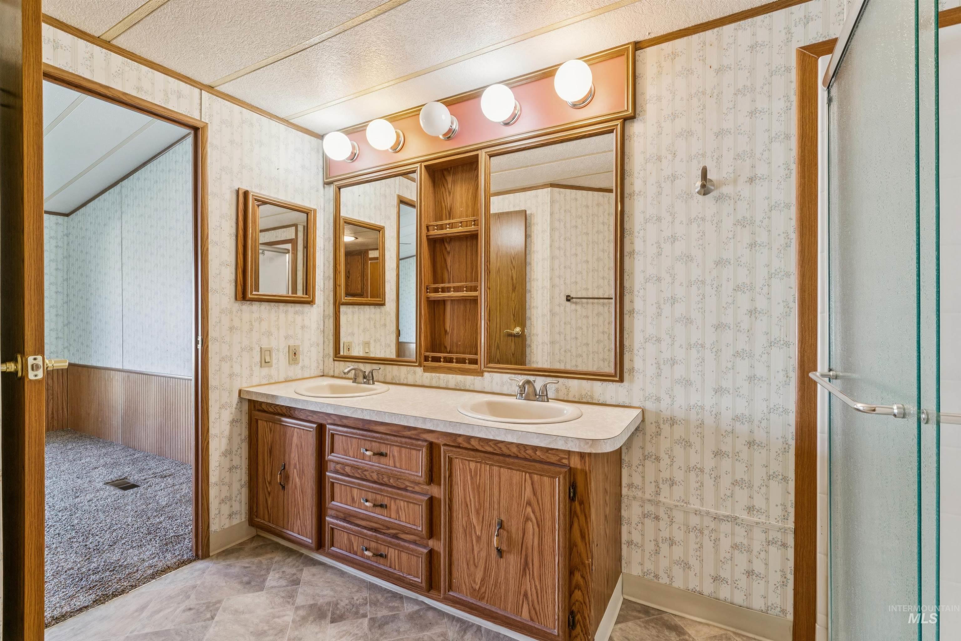 Full bathroom featuring double vanity, wallpapered walls, and a shower with door