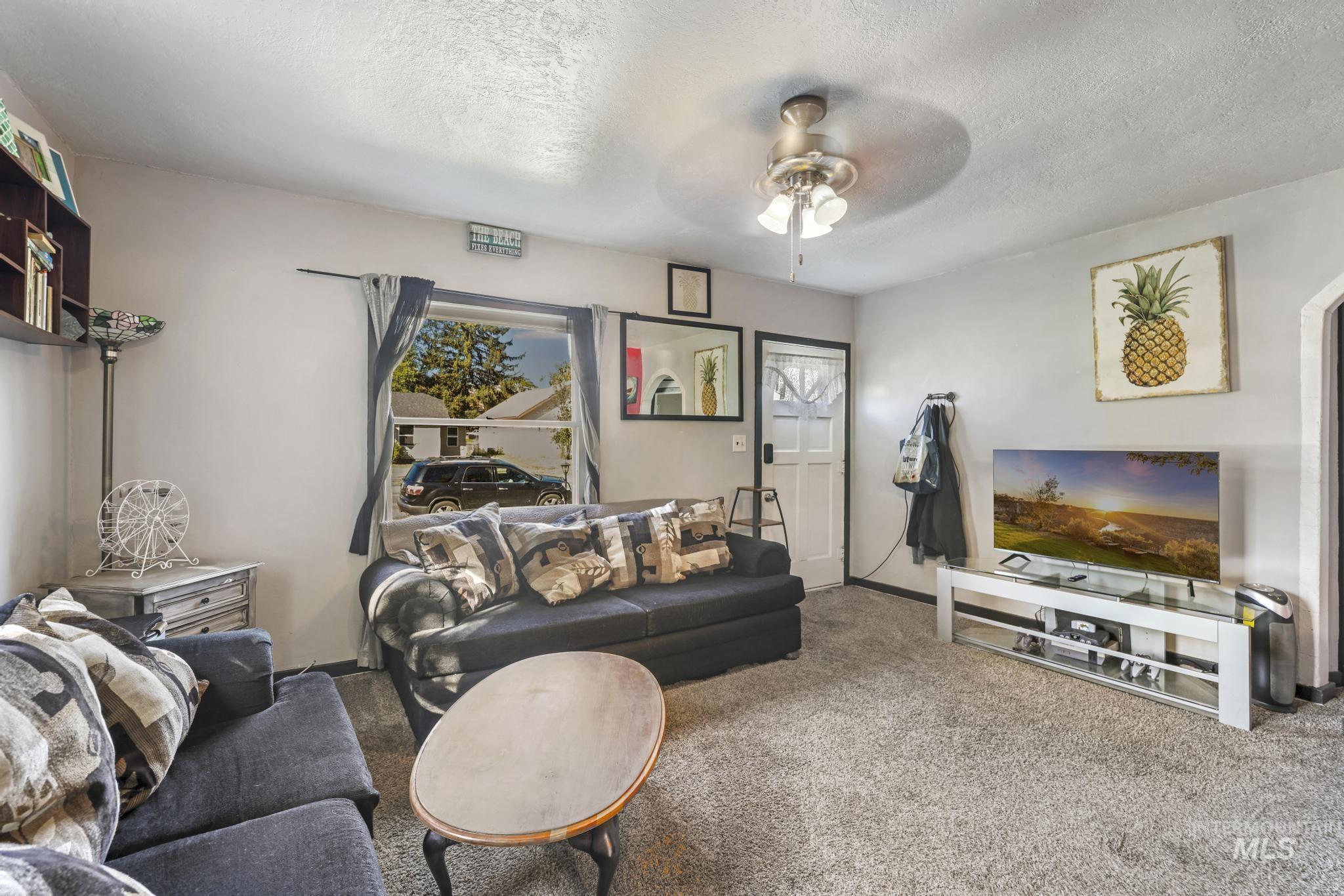 Carpeted living room with a textured ceiling and ceiling fan