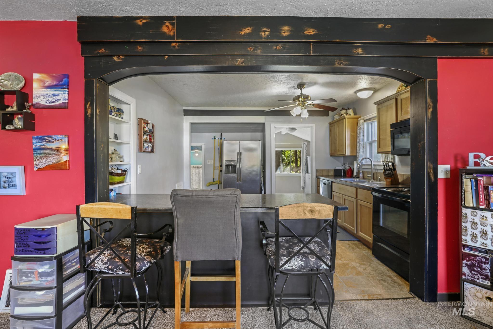 Kitchen featuring dark countertops, arched walkways, black appliances, a breakfast bar area, and a textured ceiling