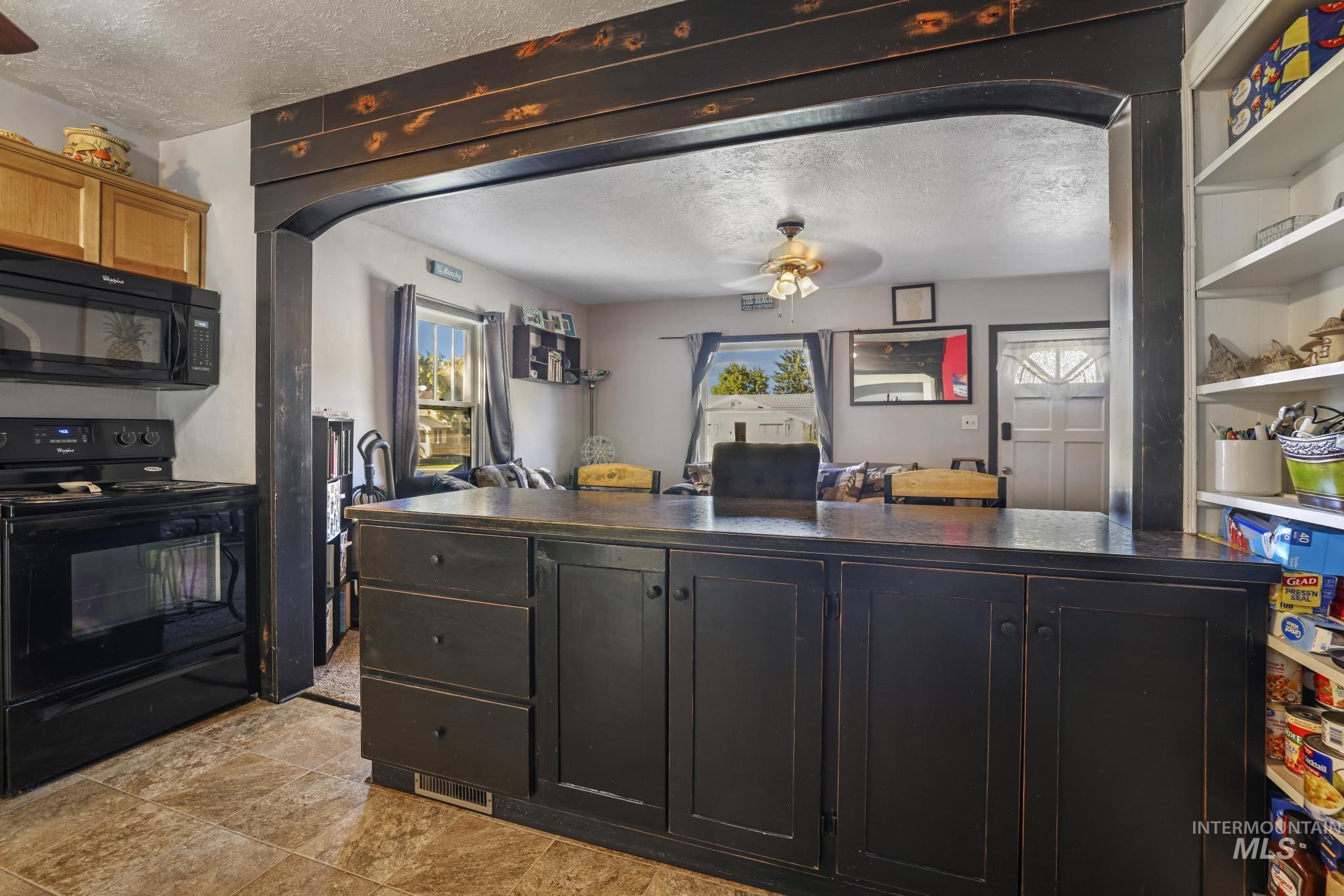 Kitchen with black appliances, a textured ceiling, arched walkways, ceiling fan, and dark countertops