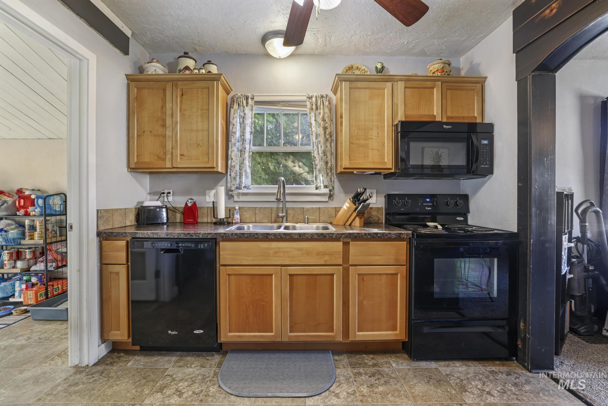Kitchen featuring black appliances, a textured ceiling, brown cabinetry, a ceiling fan, and arched walkways
