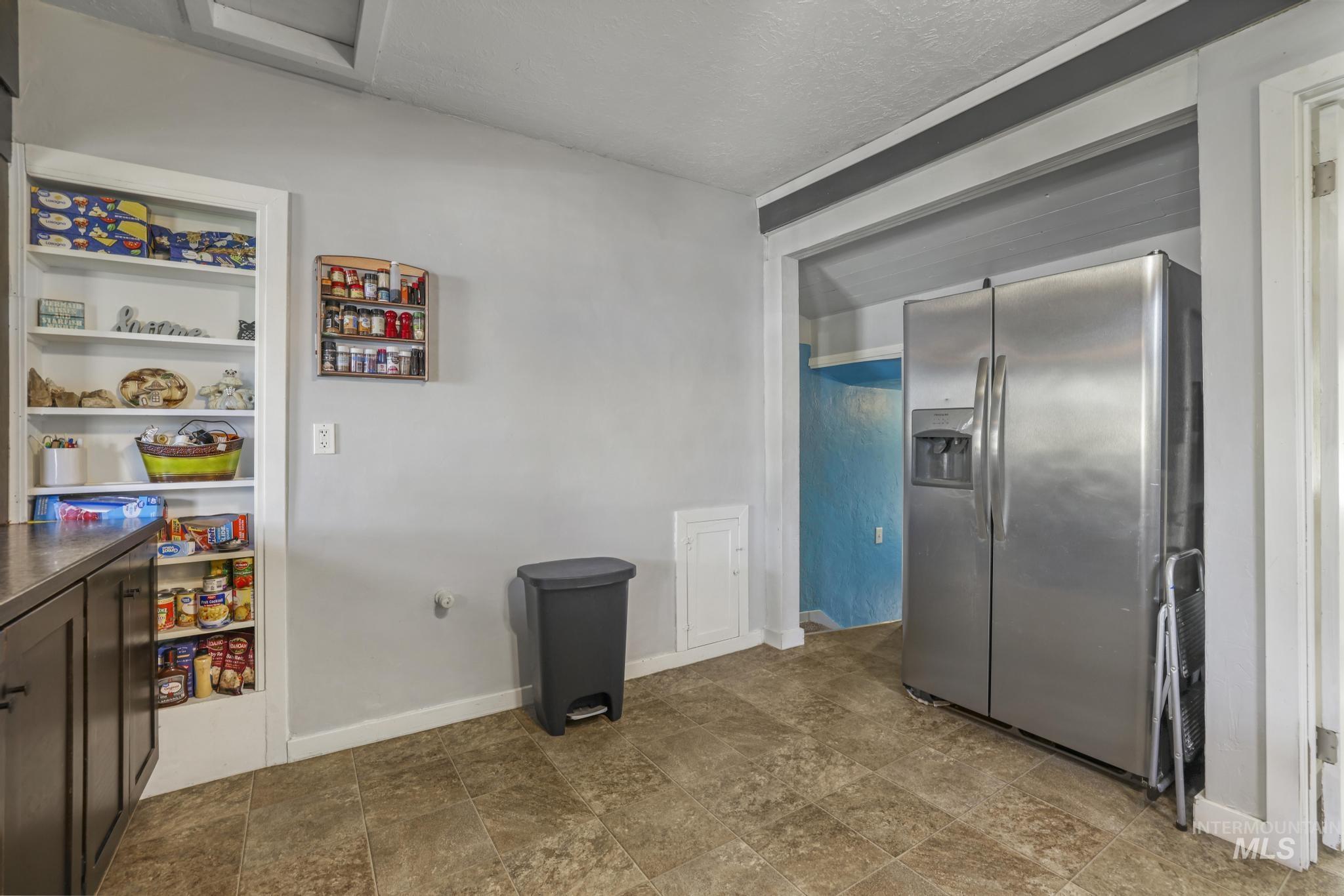 Kitchen with stainless steel fridge, a textured ceiling, dark brown cabinetry, open shelves, and dark countertops