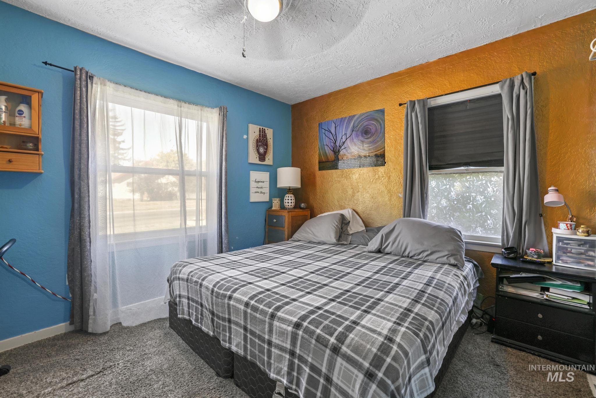 Bedroom featuring a textured wall, a textured ceiling, dark carpet, and a ceiling fan
