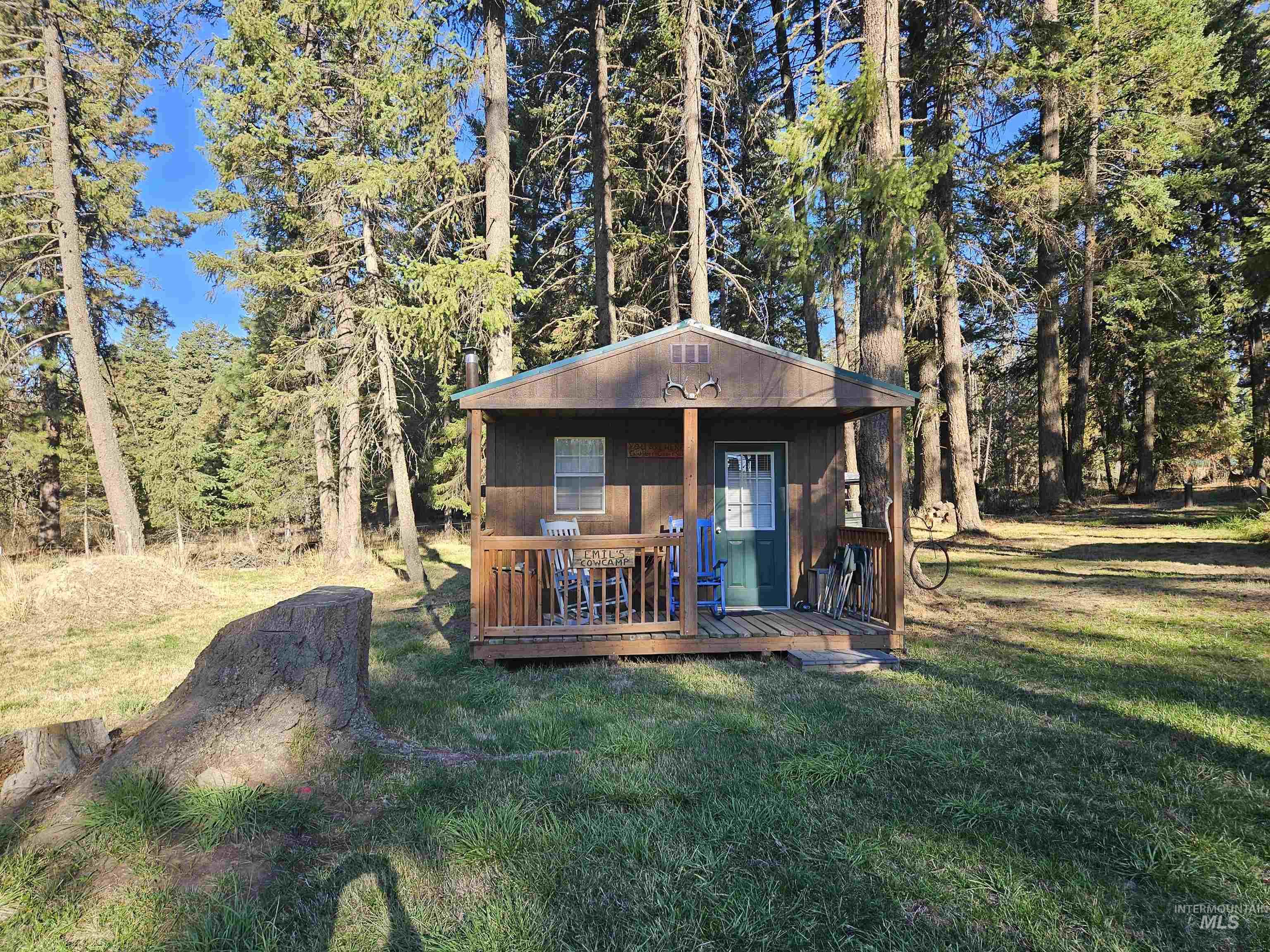 View of front of house with a deck, an outdoor structure, a front yard, and a wooded view