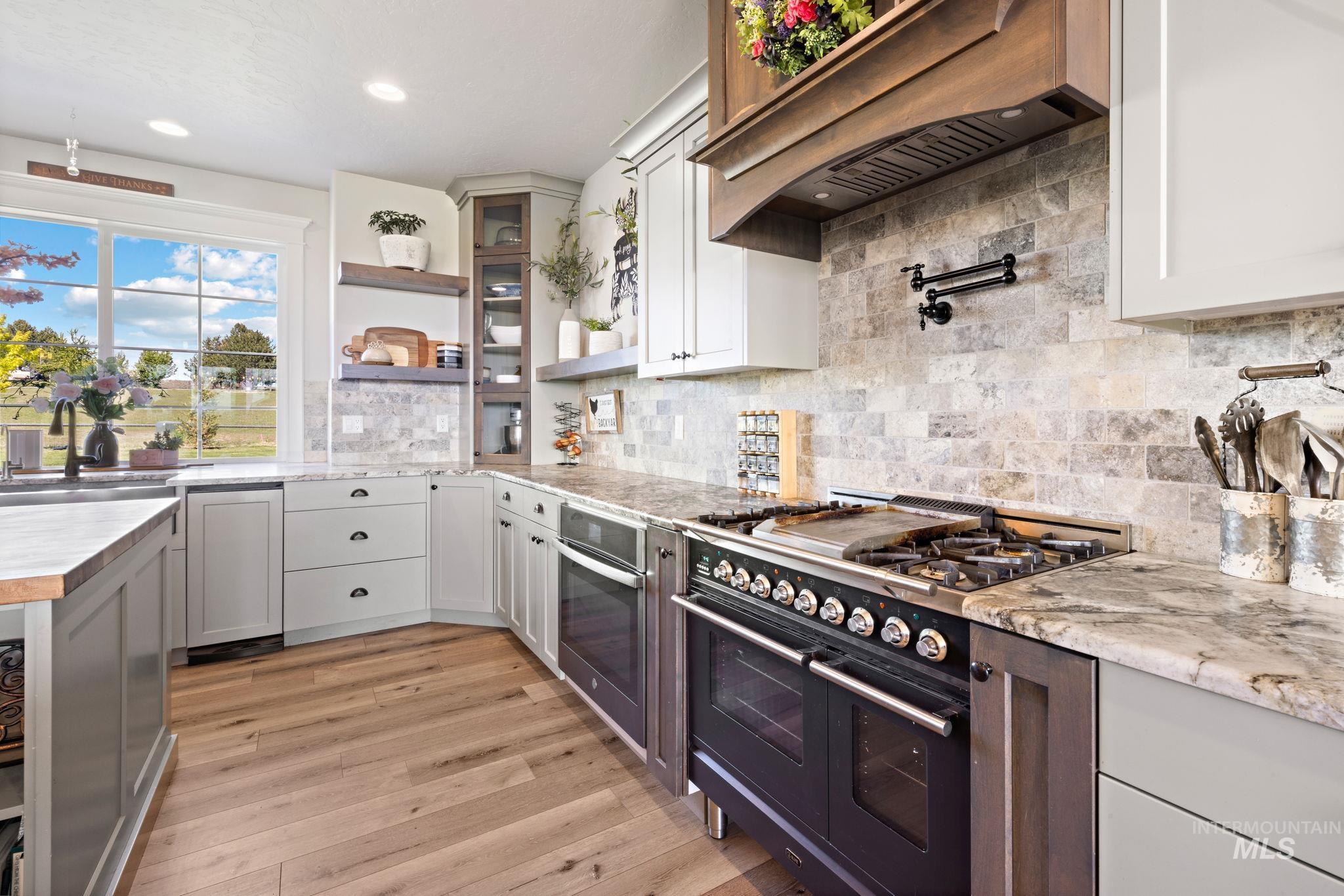 Kitchen with double oven range, open shelves, decorative backsplash, custom range hood, and white cabinetry