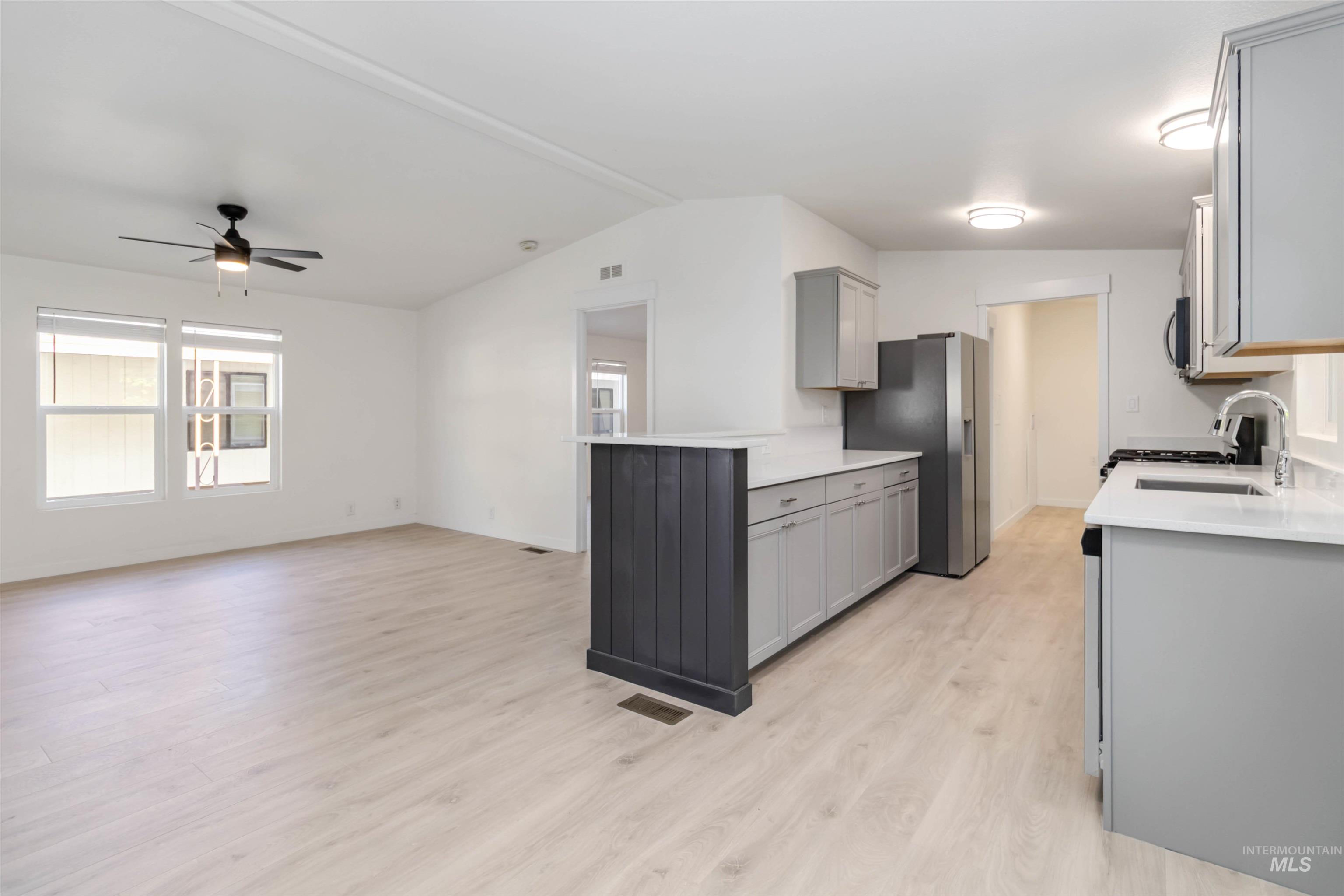Kitchen featuring gray cabinets, light wood-style flooring, stainless steel appliances, lofted ceiling, and ceiling fan