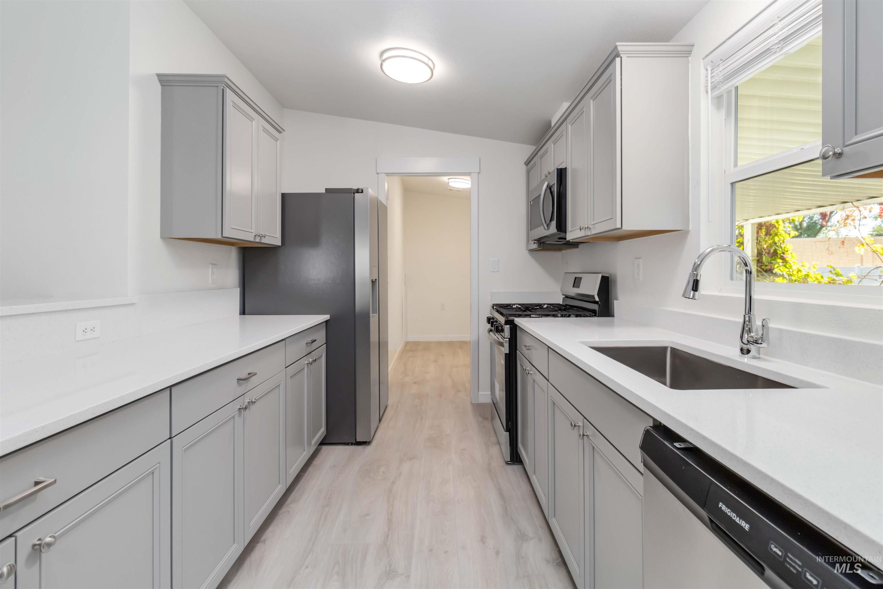 Kitchen featuring gray cabinets, appliances with stainless steel finishes, light wood finished floors, light stone countertops, and vaulted ceiling