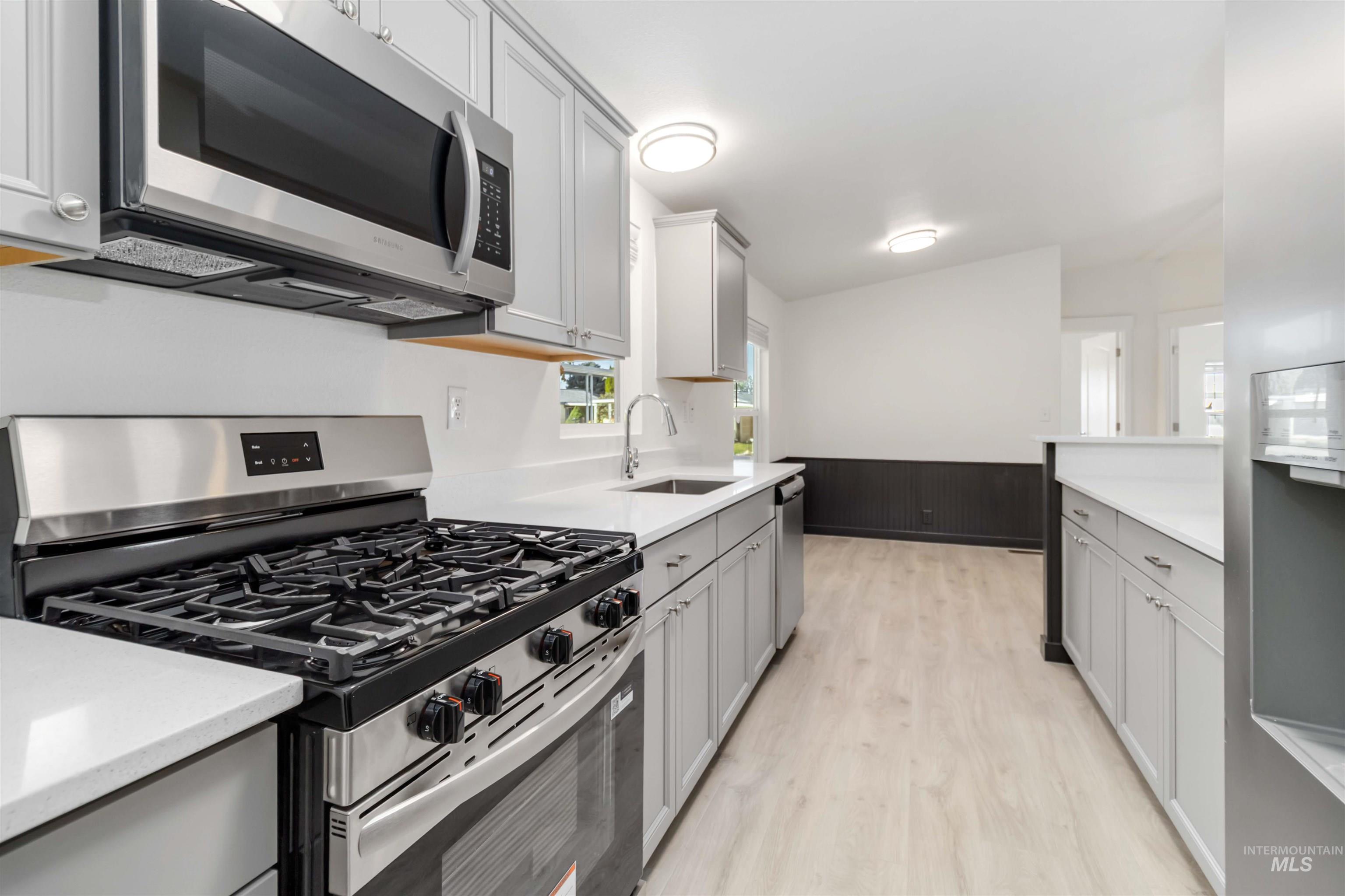 Kitchen featuring appliances with stainless steel finishes, wainscoting, light wood-style flooring, gray cabinetry, and wooden walls