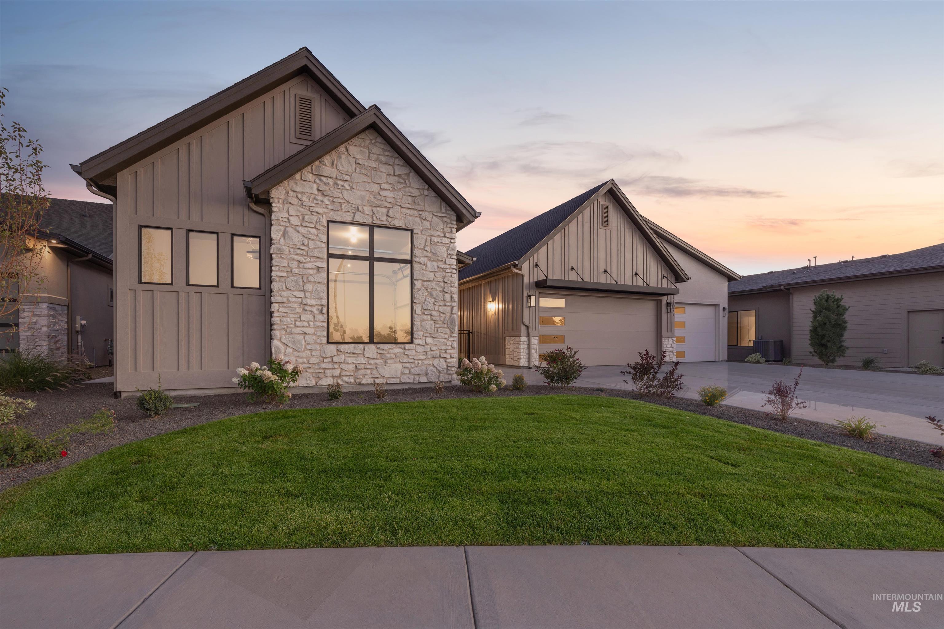 Modern farmhouse style home featuring board and batten siding, stone siding, driveway, a lawn, and a garage