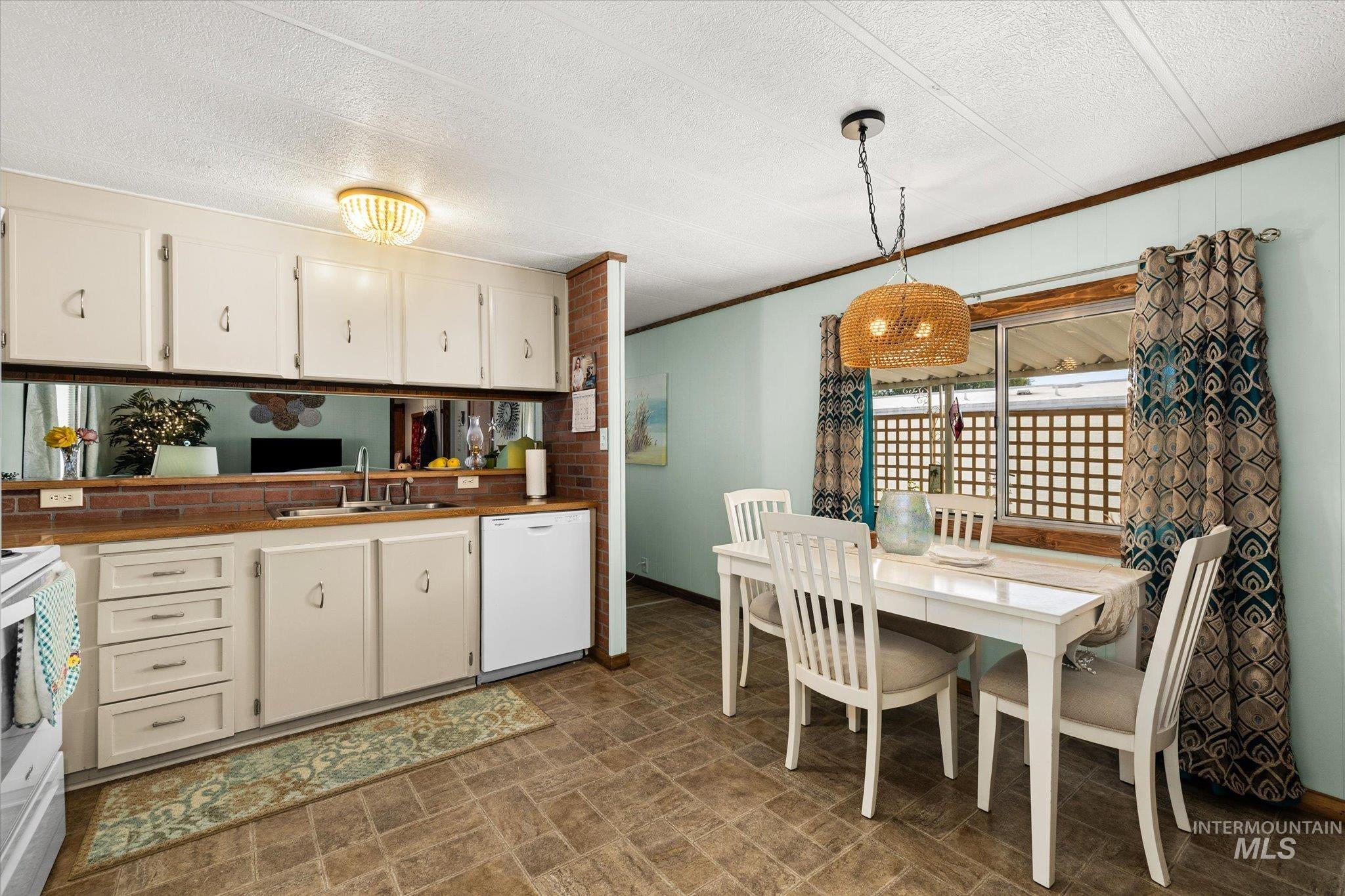 Kitchen featuring pendant lighting, white appliances, crown molding, white cabinetry, and a textured ceiling