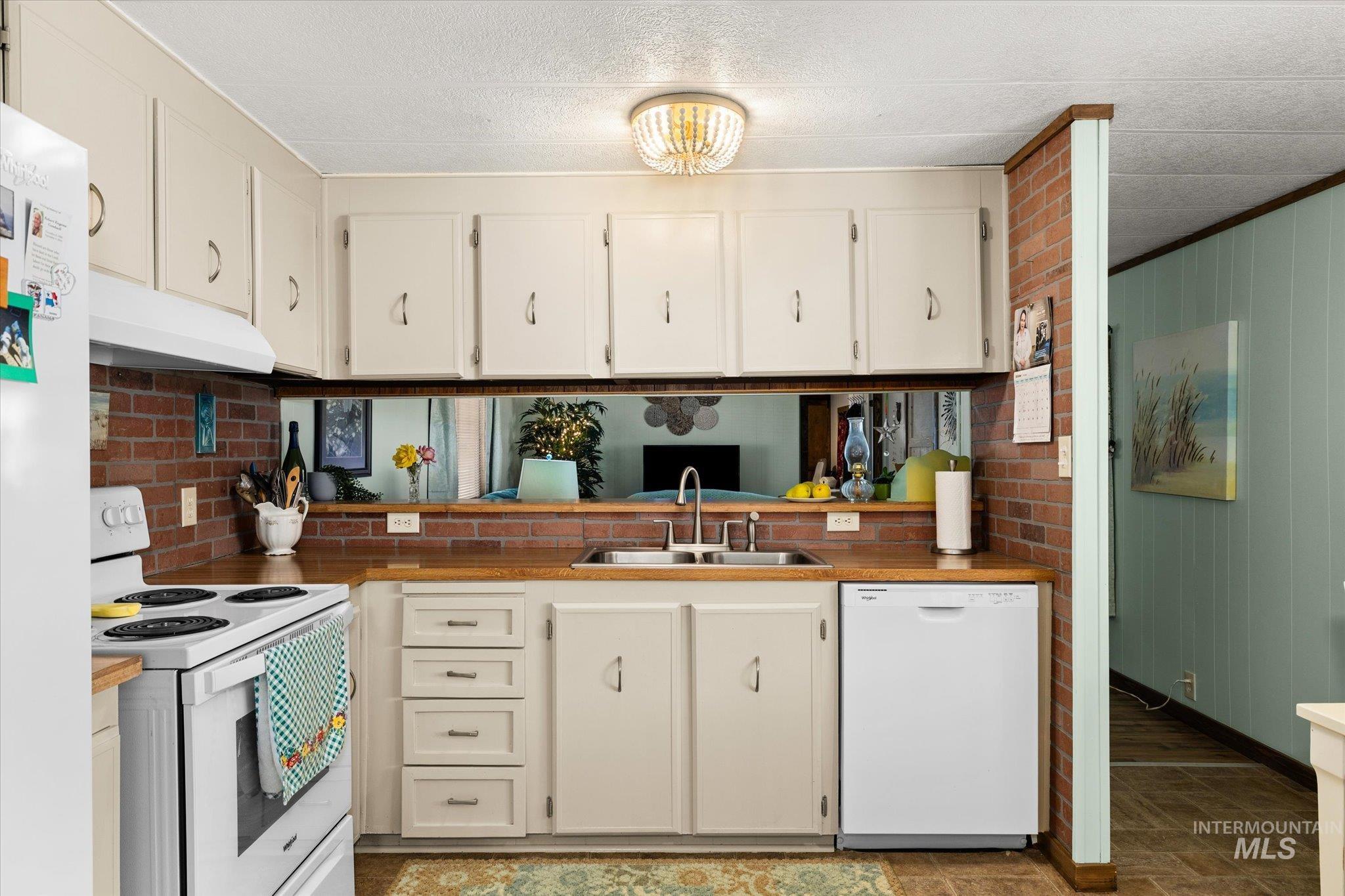 Kitchen featuring white appliances, under cabinet range hood, white cabinetry, wood walls, and a textured ceiling