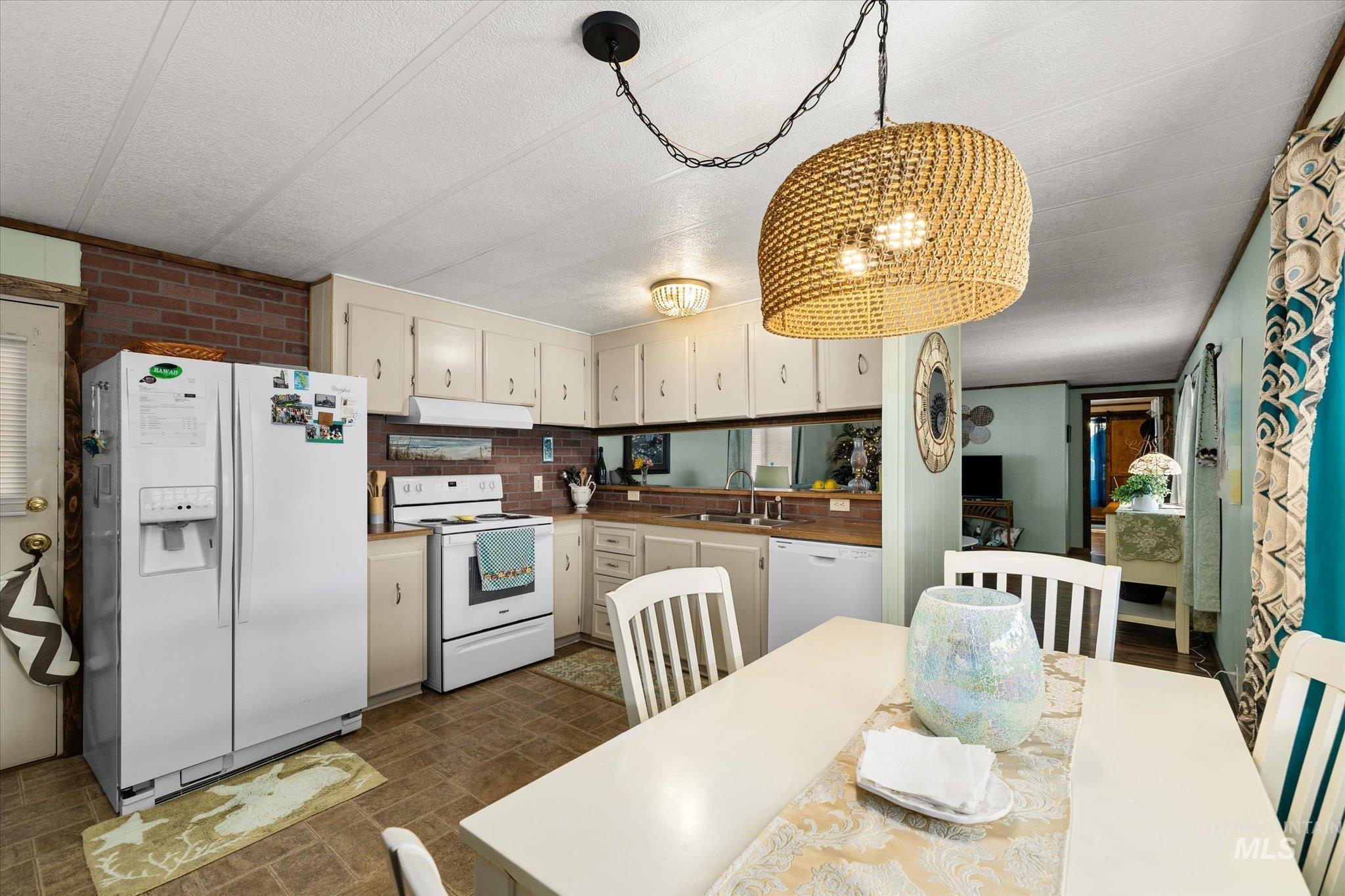 Kitchen featuring white appliances, cream cabinetry, pendant lighting, decorative backsplash, and under cabinet range hood