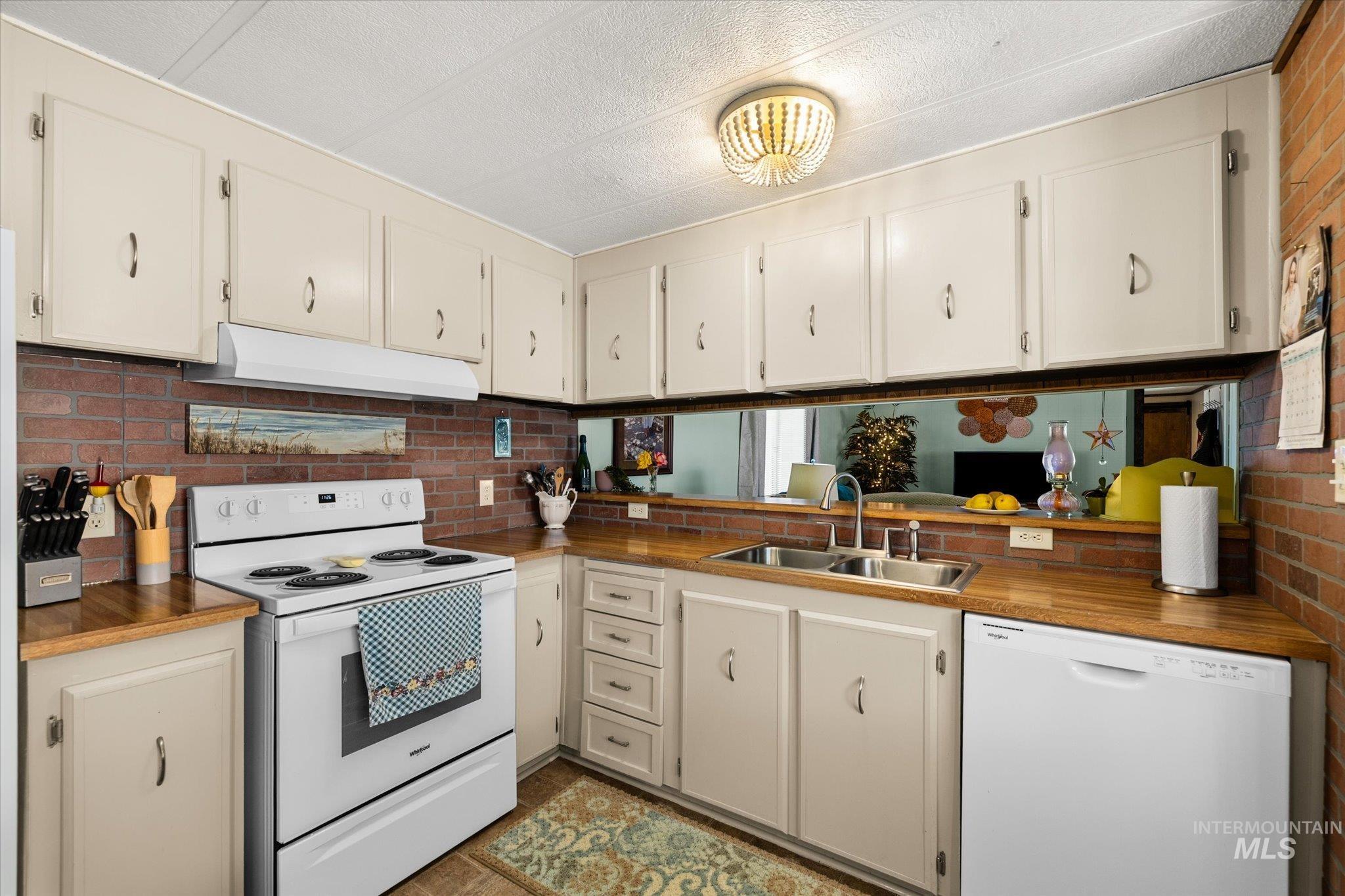 Kitchen featuring white appliances, under cabinet range hood, wooden counters, cream cabinetry, and a textured ceiling