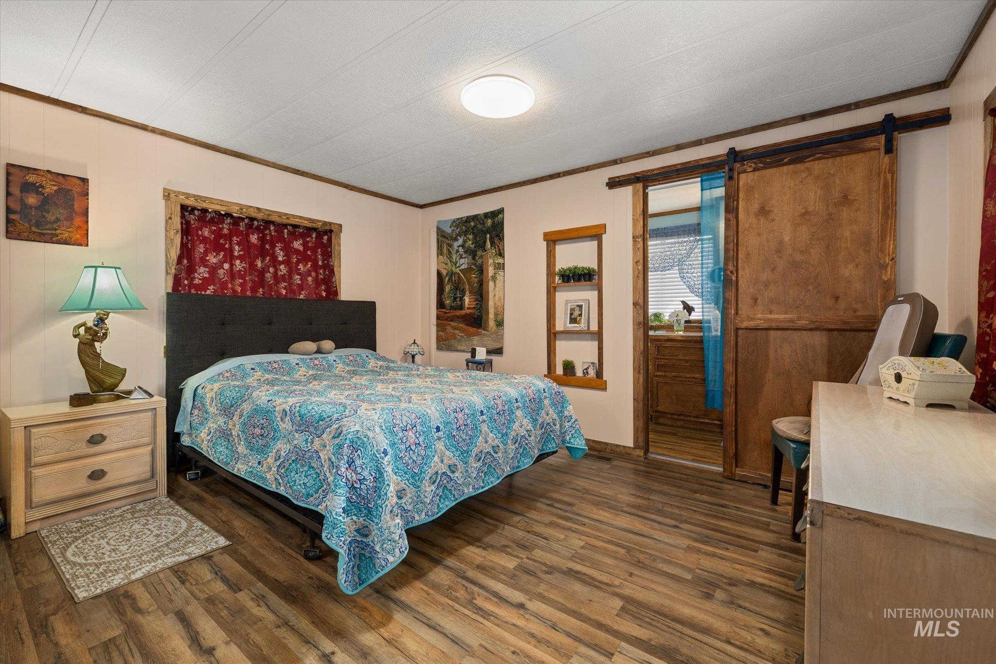 Bedroom featuring a barn door, ornamental molding, and dark wood finished floors