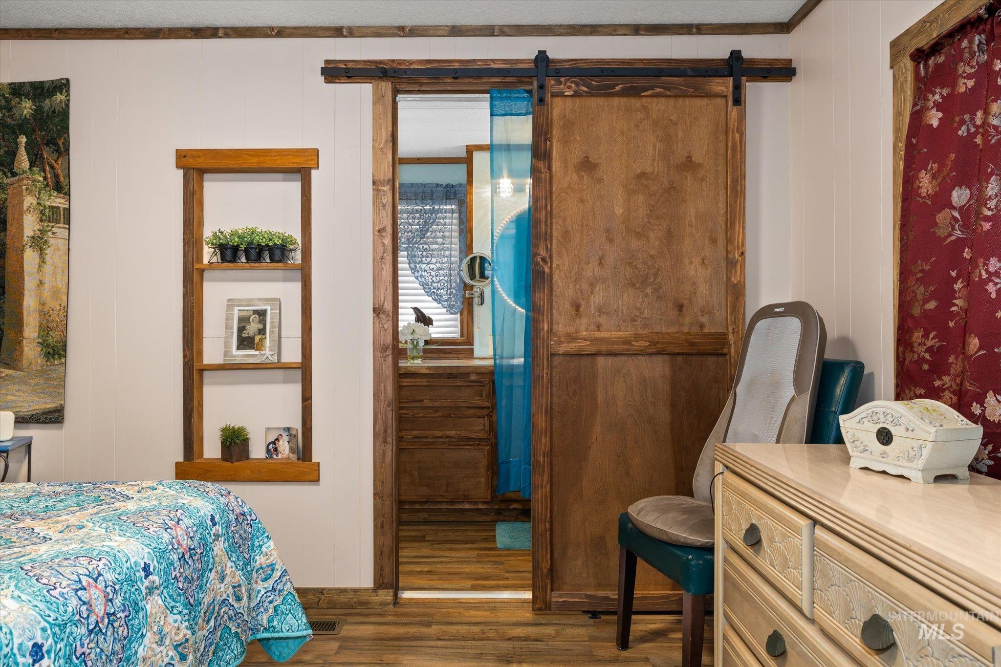 Bedroom with dark wood-style flooring, a barn door, and wood walls