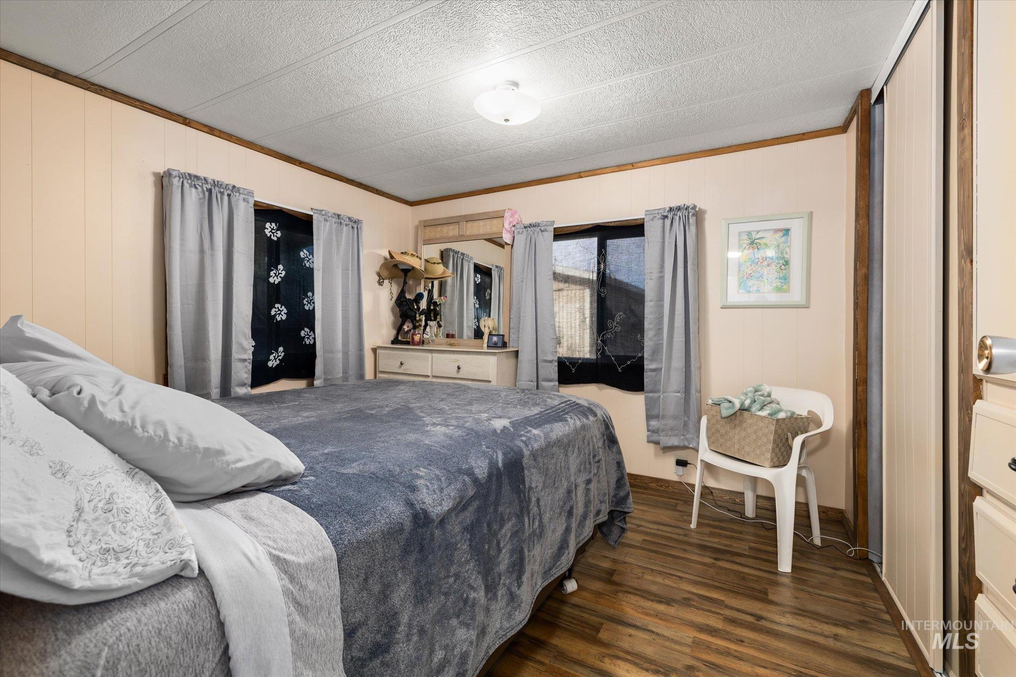 Bedroom with dark wood-type flooring, ornamental molding, and wood walls