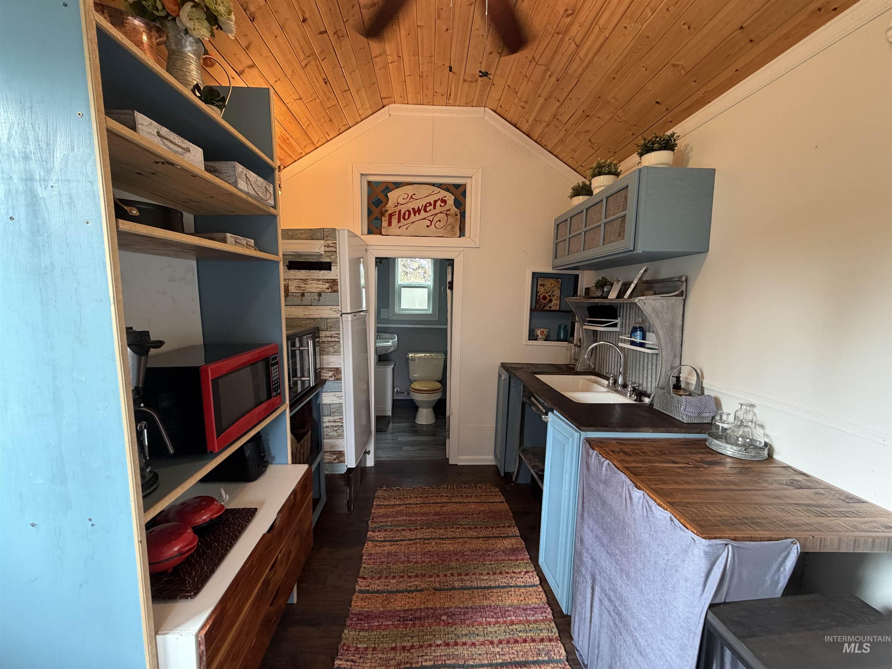Kitchen featuring dark wood-style floors, vaulted ceiling, wooden ceiling, blue cabinetry, and freestanding refrigerator