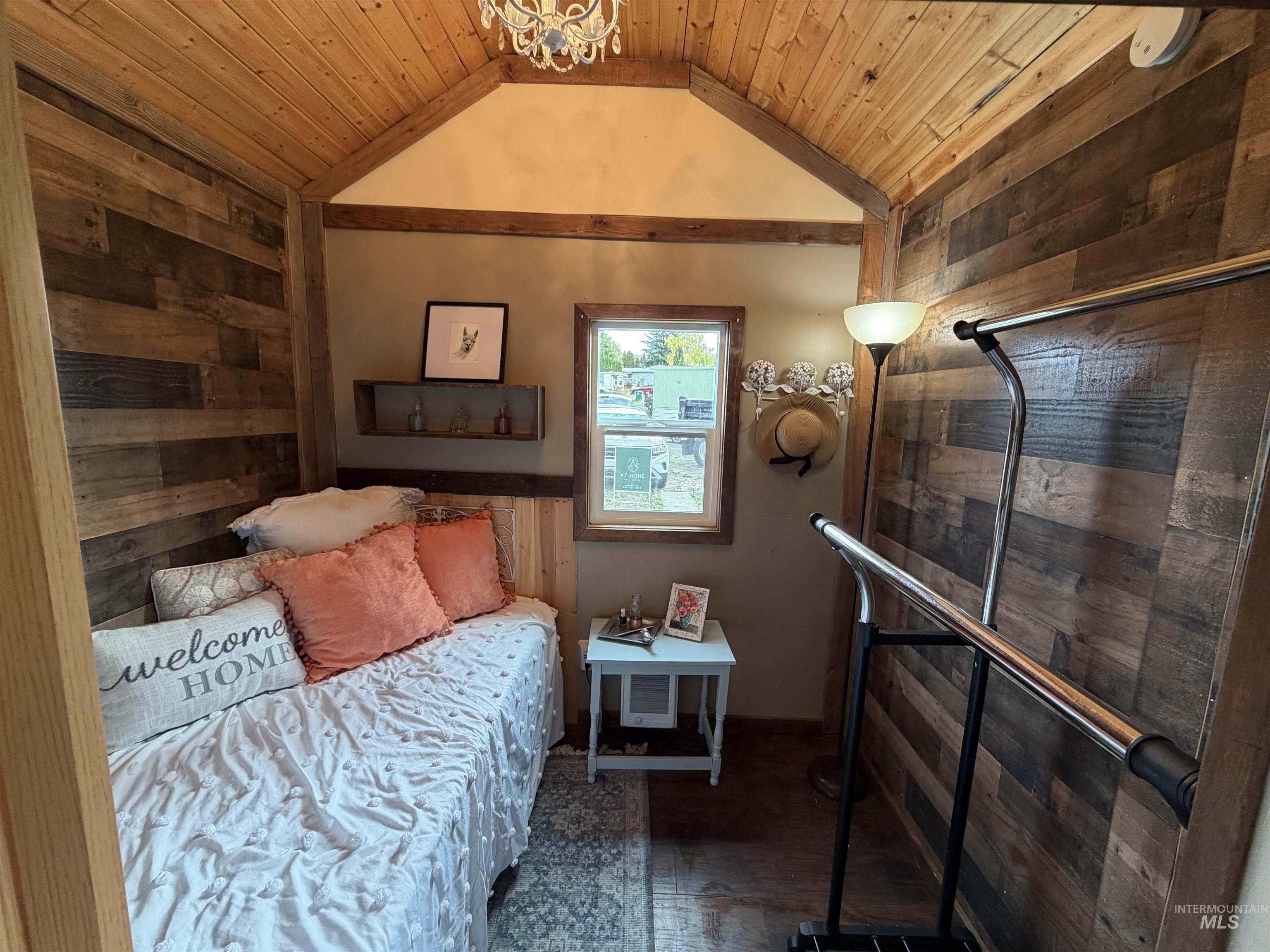 Bedroom with wood walls, vaulted ceiling, wooden ceiling, and wood finished floors