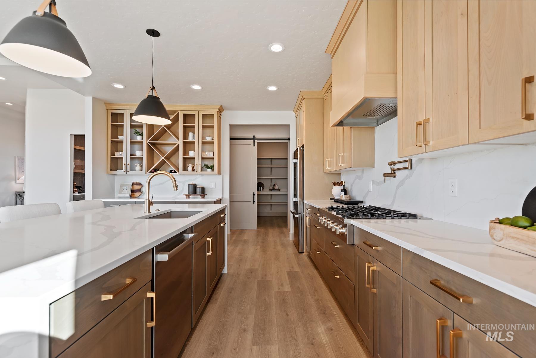 Kitchen with a barn door, light stone countertops, light wood-type flooring, glass insert cabinets, and stainless steel appliances